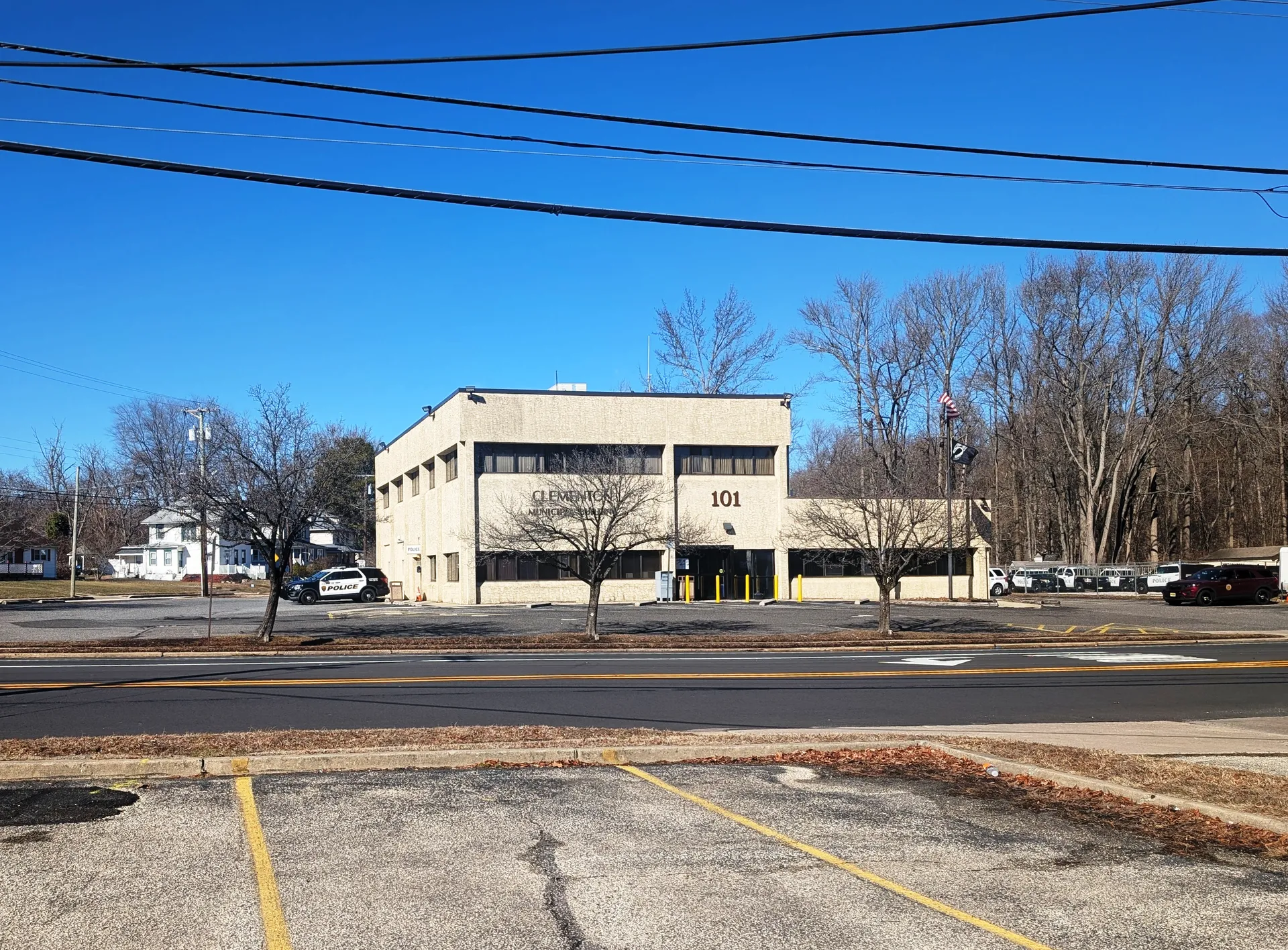 Clementon's municipal building is a two-story beige building with a flat roof, surrounded by a parking lot and bare trees.