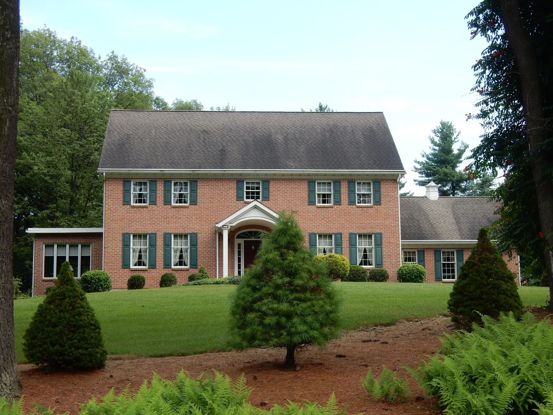 A large red-brick colonial-style home with green shutters and a landscaped front yard stands on Louisa Avenue in East Norwegian Township.