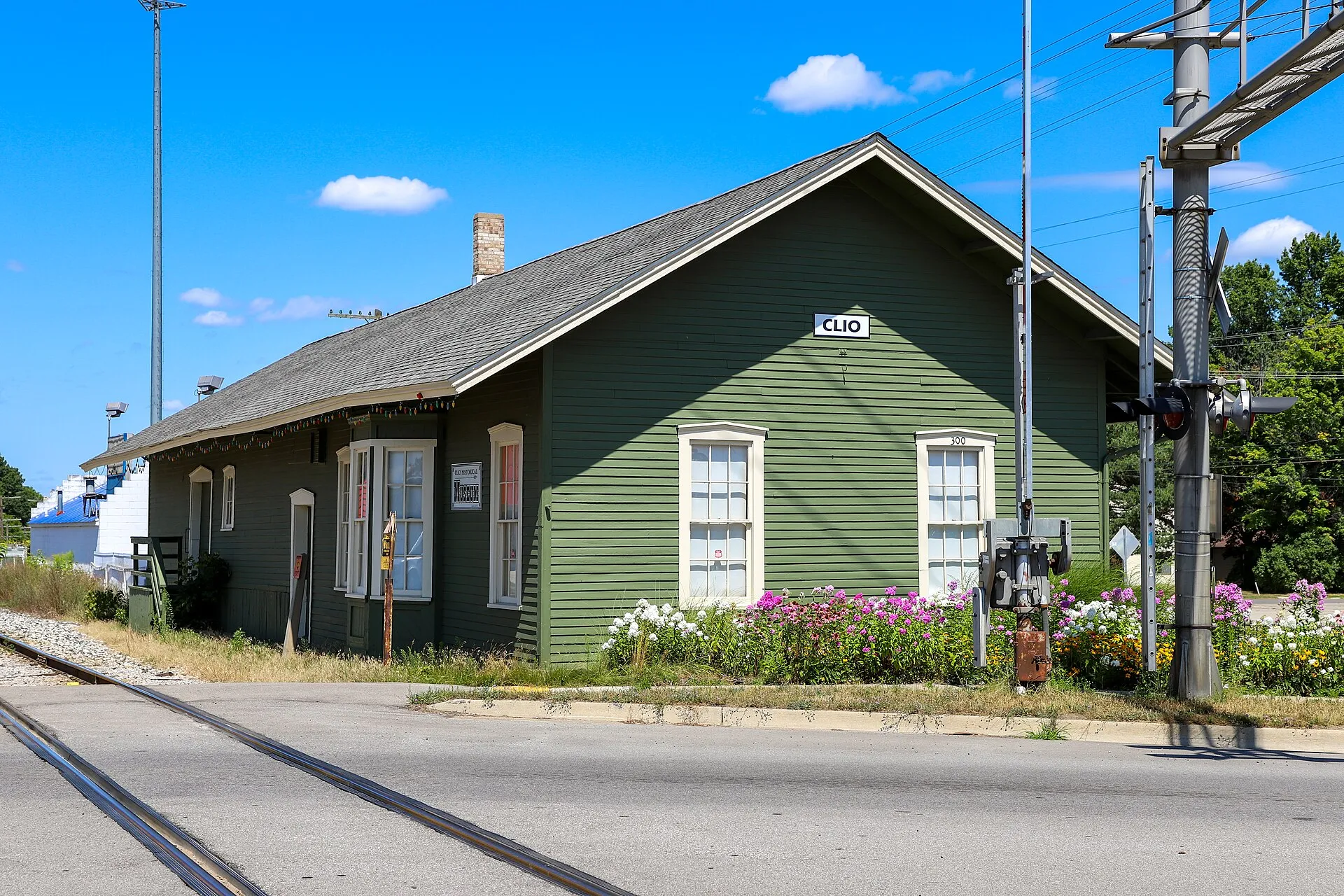 The restored Clio depot is a green wooden railroad station with white-trimmed windows and colorful flower beds along the street.