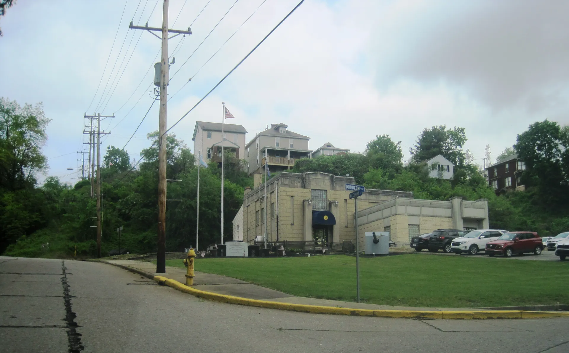 Dravosburg's American Legion Post 380 is a tan brick building with flags, seen from McClure Street beneath hillside homes.