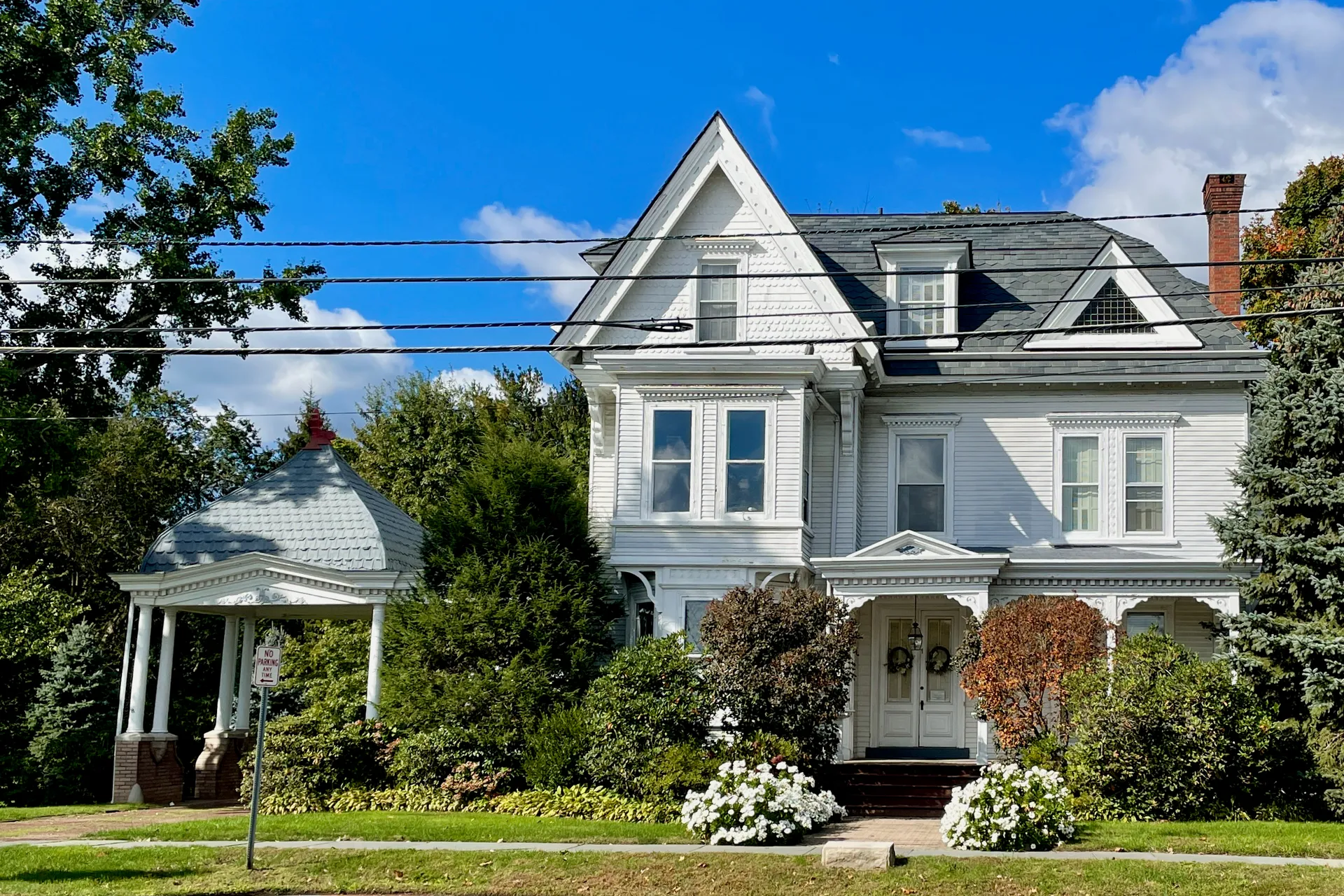 At 1 North Main Street in Cranbury, a white Victorian house with gables and a front porch stands behind flowering shrubs.