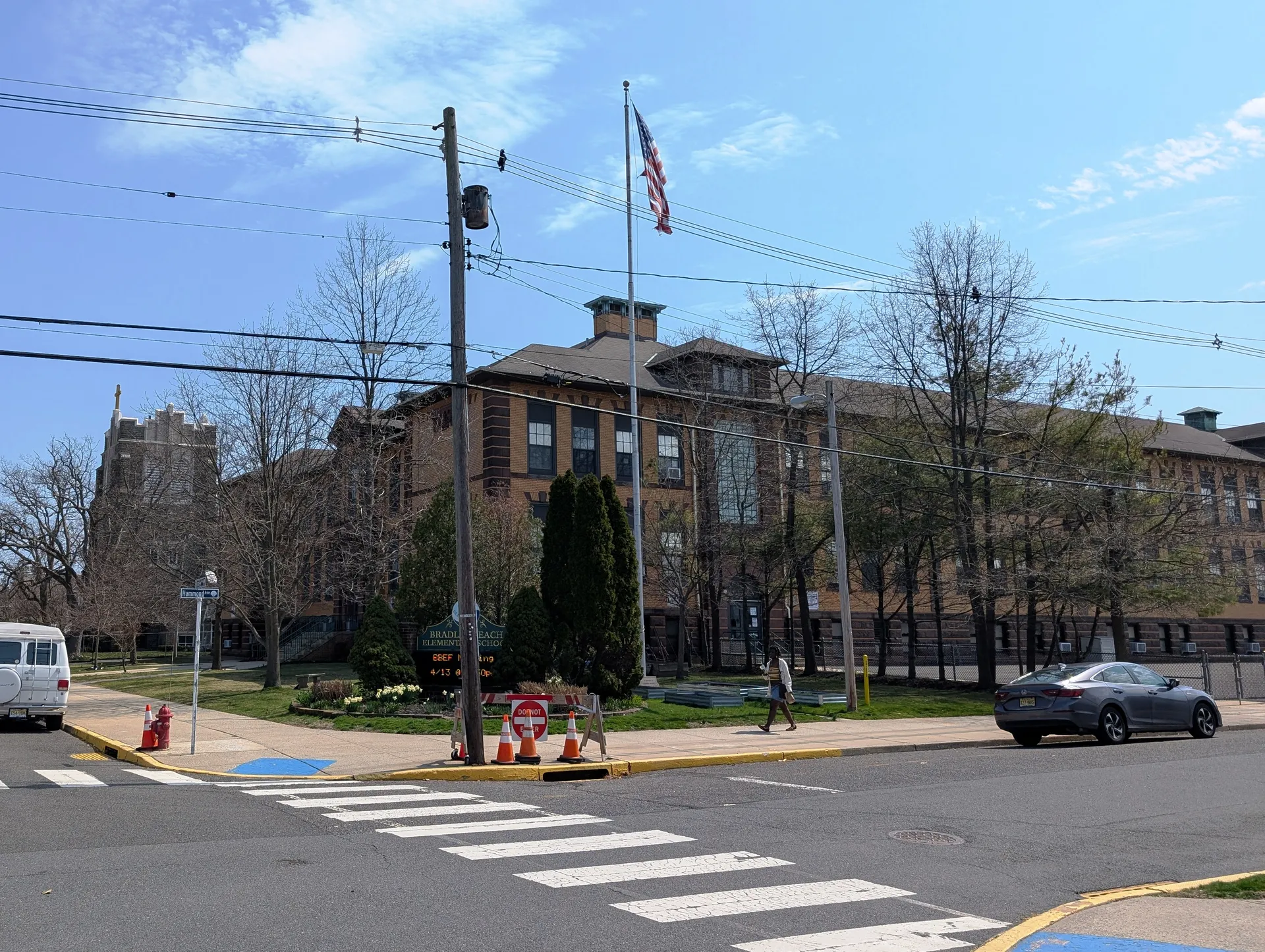 Bradley Beach Elementary School is a red brick building with a flag out front and a painted crosswalk leading to the entrance.