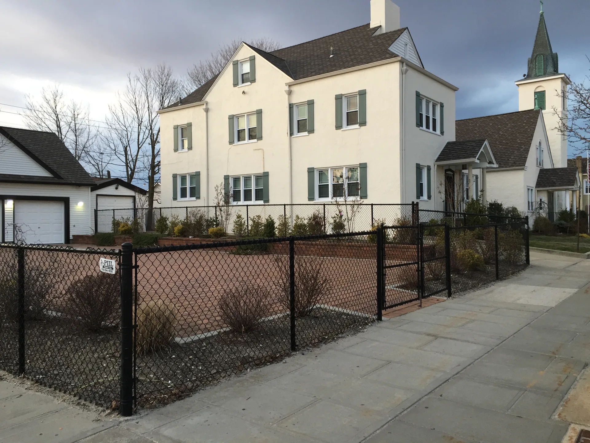 Historic white two-story building behind an iron fence in Island Park, New York.