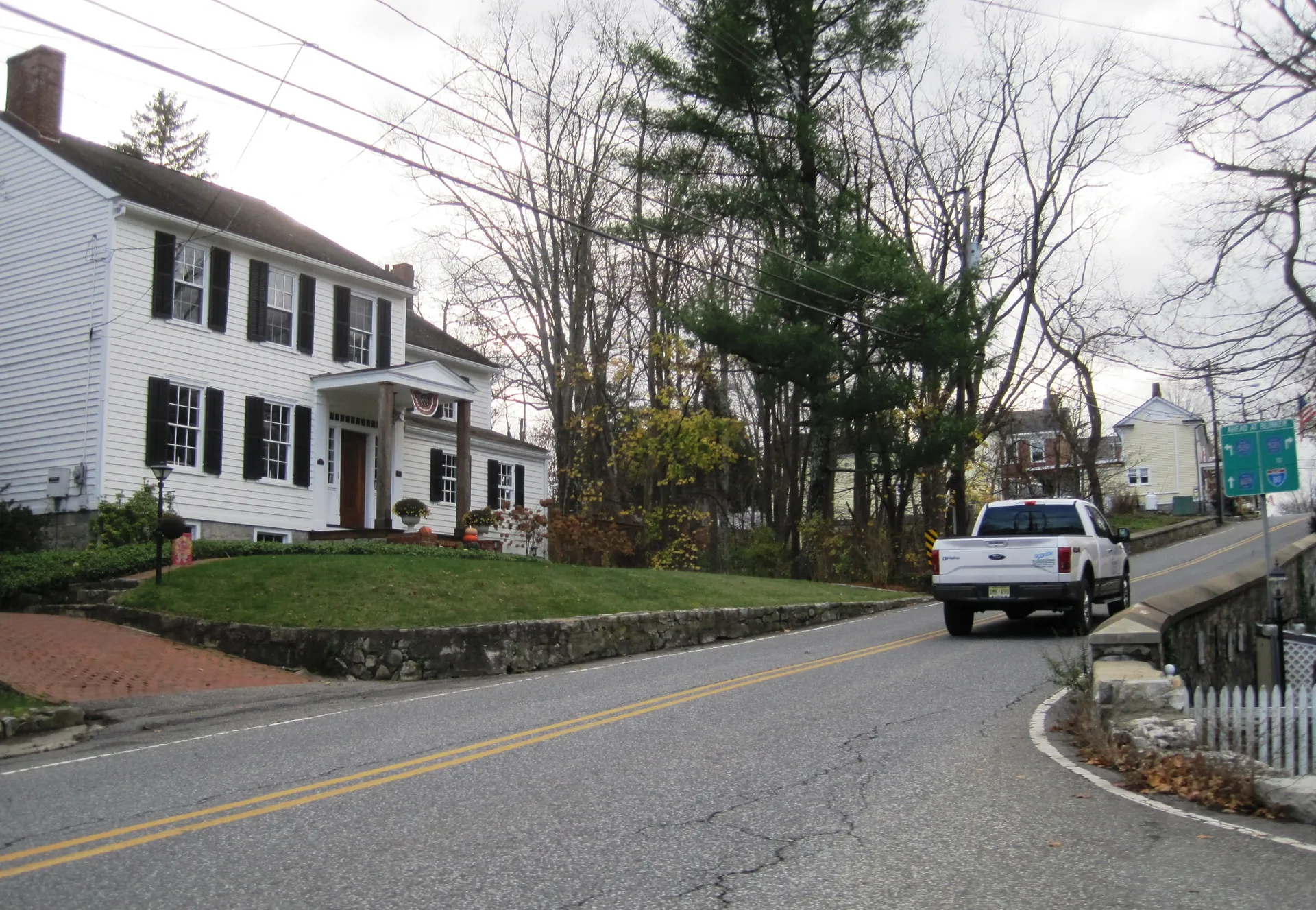 A quiet street in Hope passes white houses and tall evergreens, with a pickup truck parked by the curb.