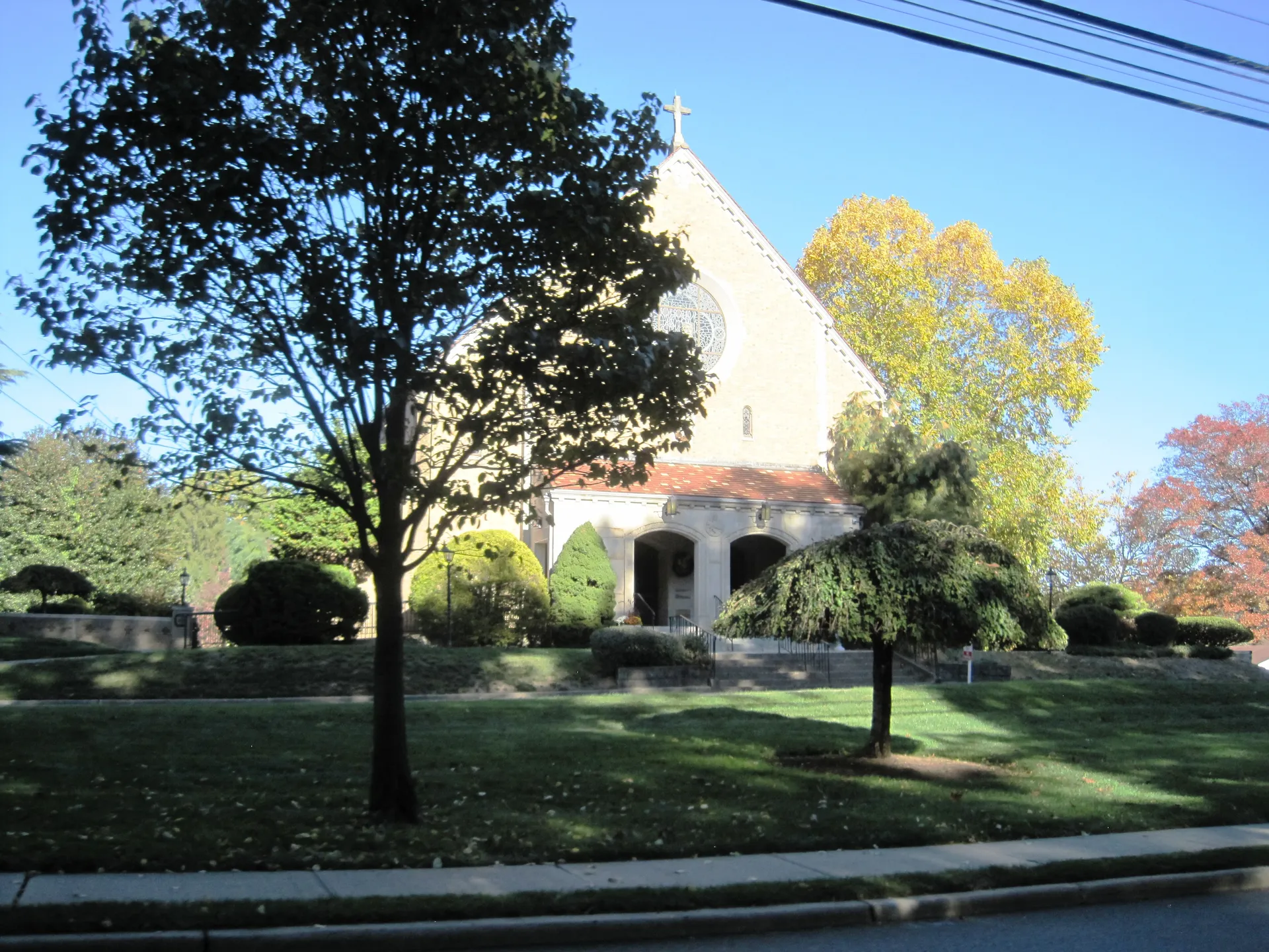 St. Luke's RC Church in Ho-Ho-Kus is a stucco church with a tile roof, set behind palms and a shaded lawn.