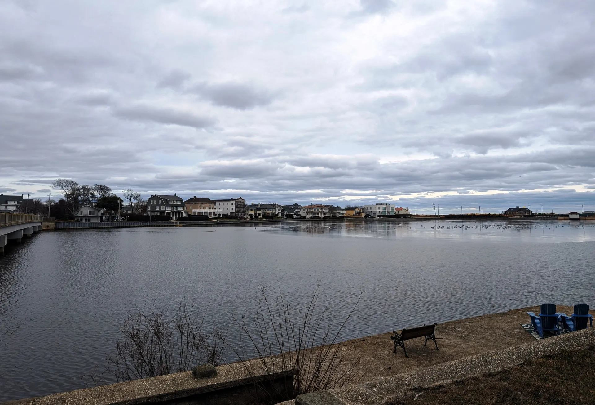 Loch Arbour lies along the far shore of a calm lake, viewed across the water on an overcast winter day.