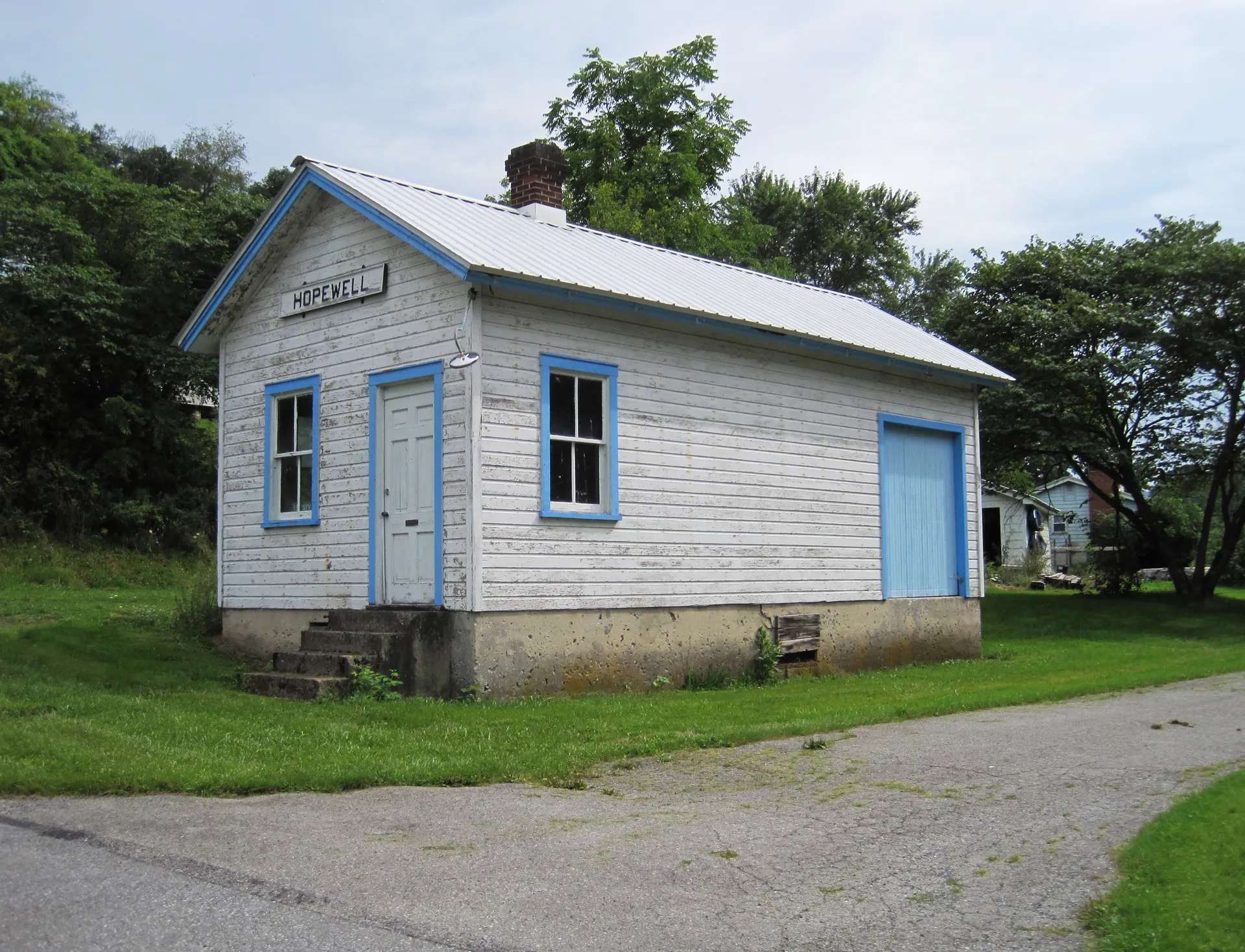 Hopewell's former train station is a small white board-and-batten building with a blue door, now on a quiet lawn.