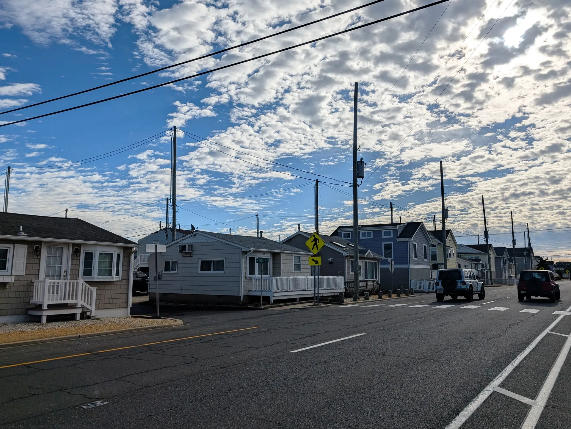 A row of small one-story bungalows with white railings lines the street in Dover Beaches North under a sky of broken clouds.