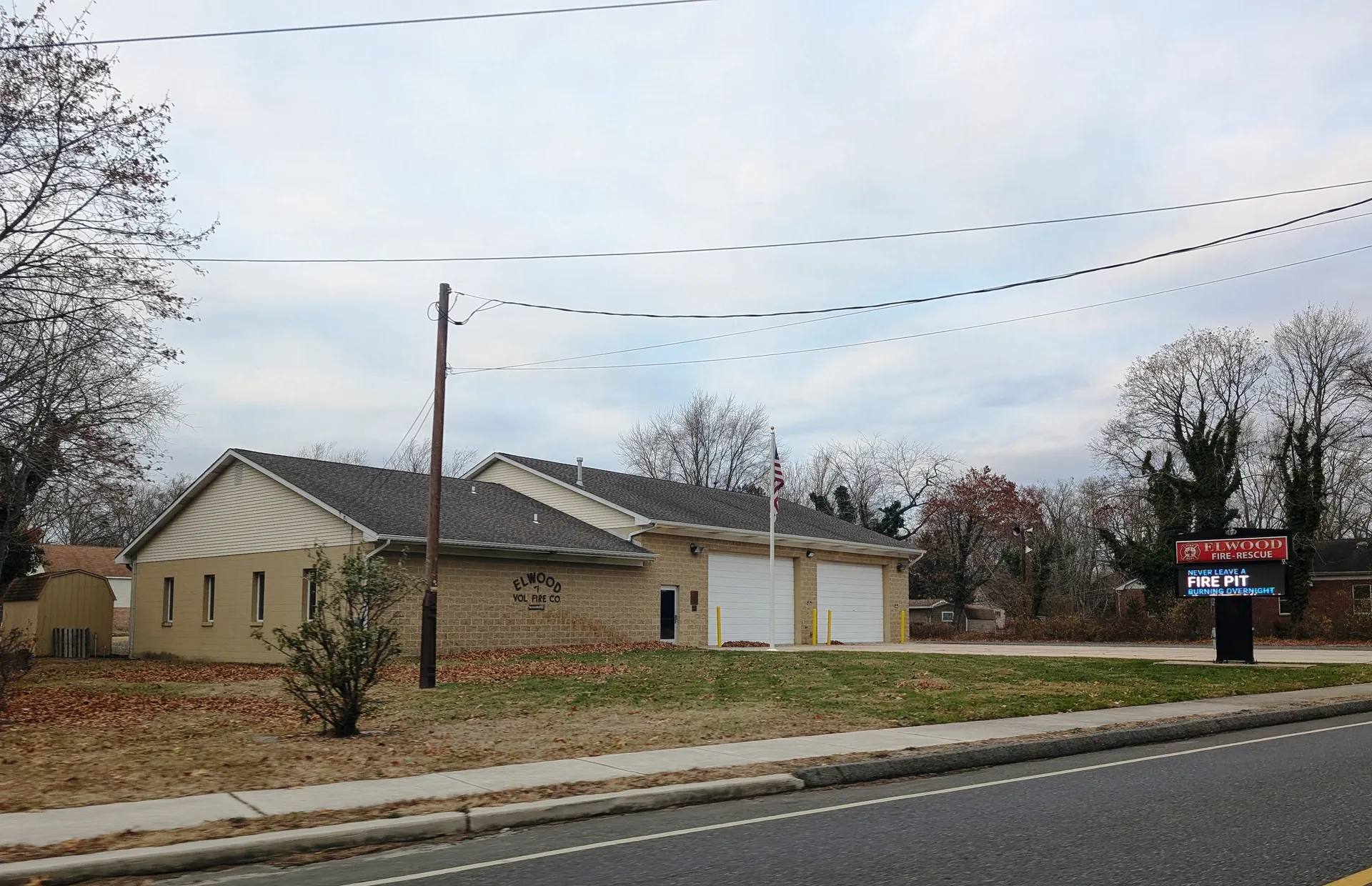Elwood's fire and rescue station is a tan building with two white bay doors next to a low brick wing along the road.