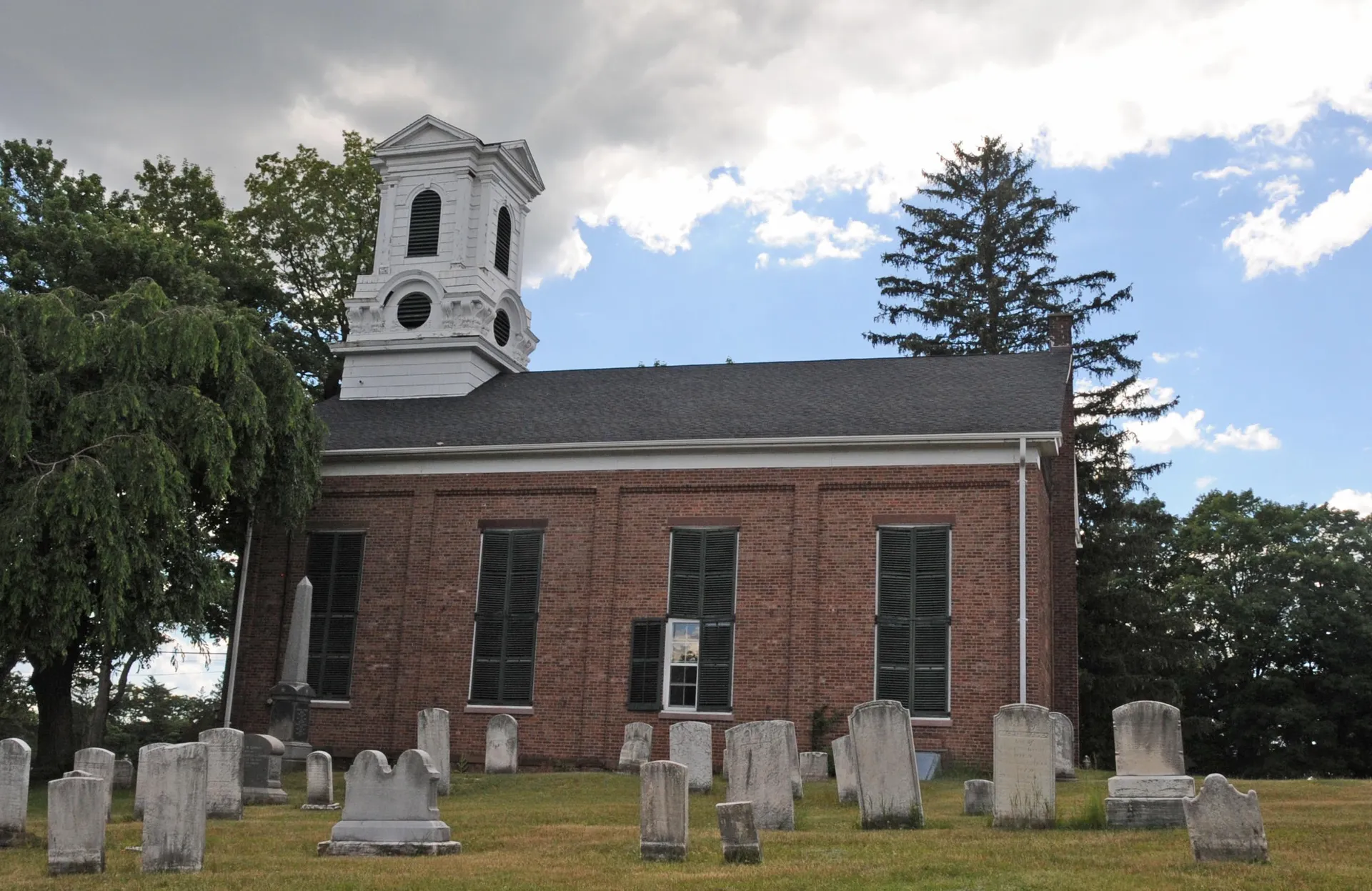 Historic brick church with a white cupola and churchyard in New Hempstead, New York.