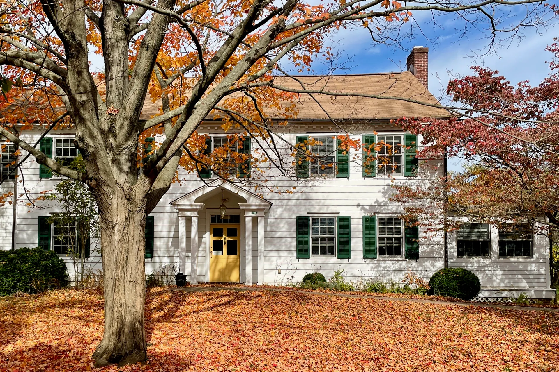 The Thomas Lloyd House at Brookdale Farm in Lincroft is a white colonial home with green shutters, framed by orange autumn leaves.