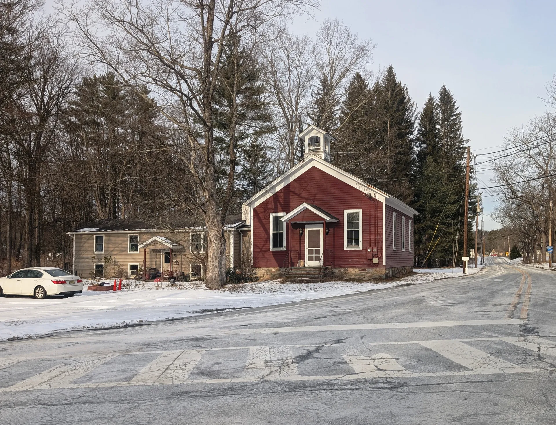 In Layton, the former schoolhouse is a small red wooden building with white trim beside a snowy lot.