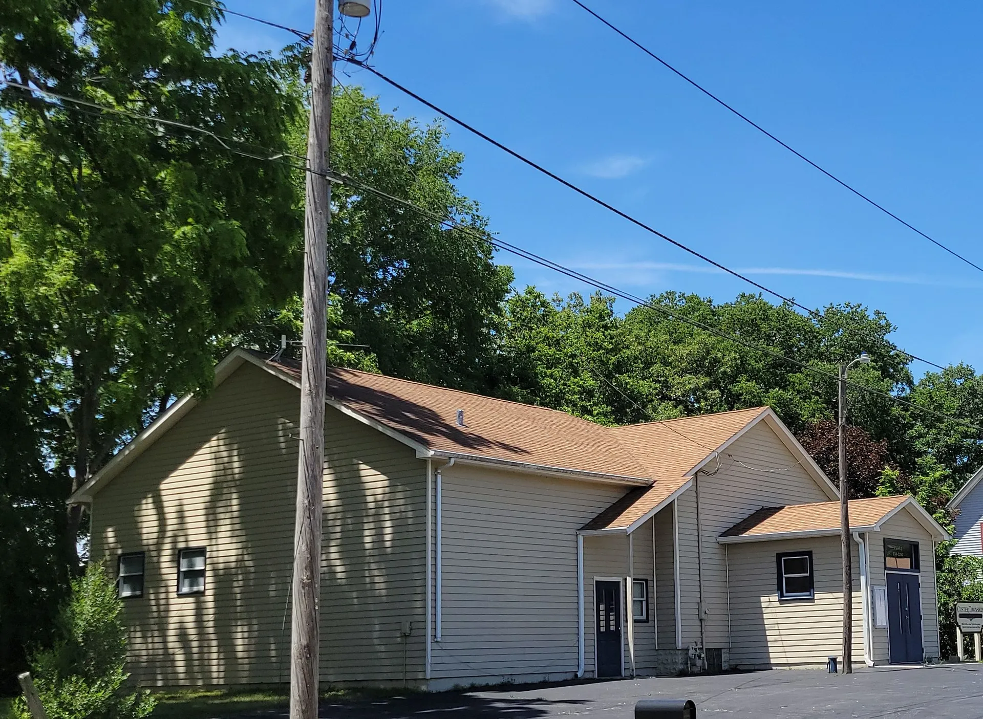 Custer Township's building is a cream-sided structure with a brown roof and a side entry door, shaded by tall trees and overhead wires.