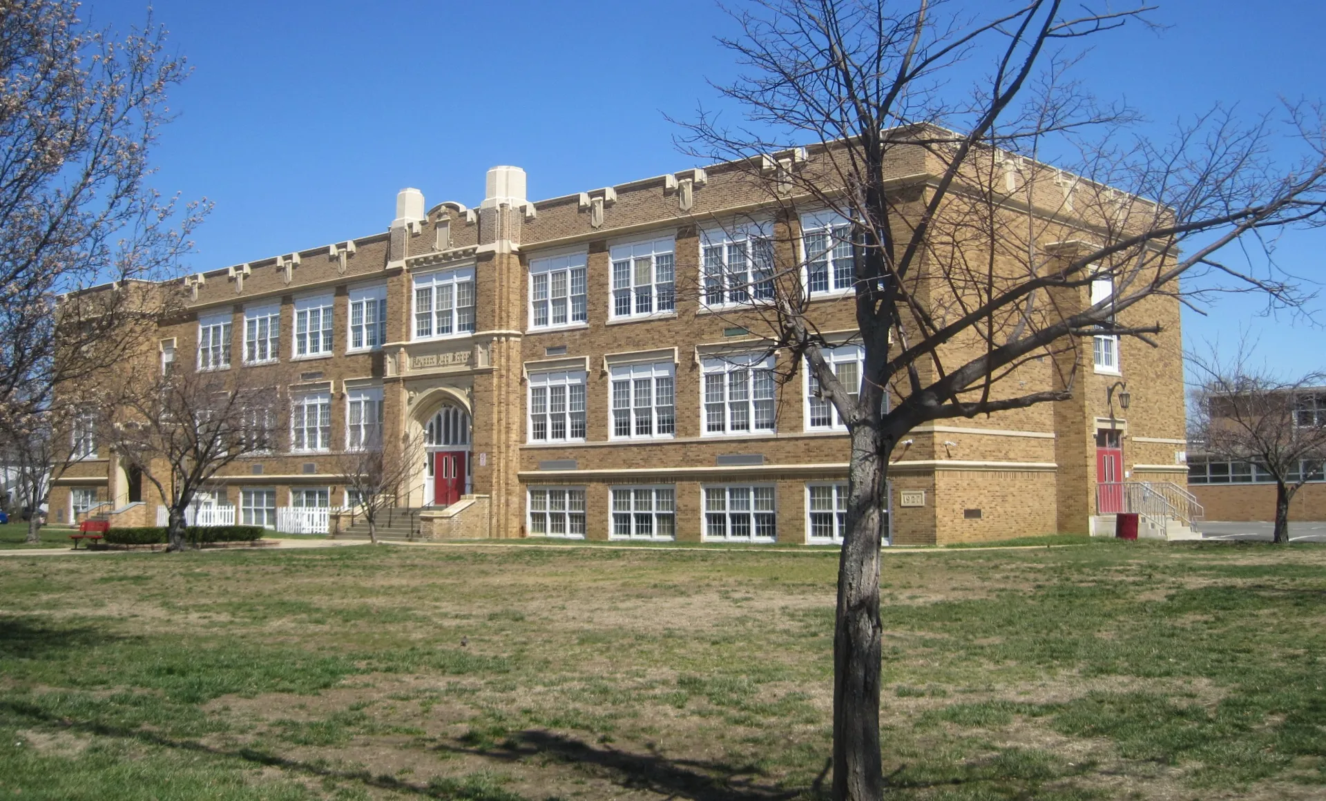Keyport High School is a three-story yellow brick building with rows of windows, behind a lawn and bare tree.