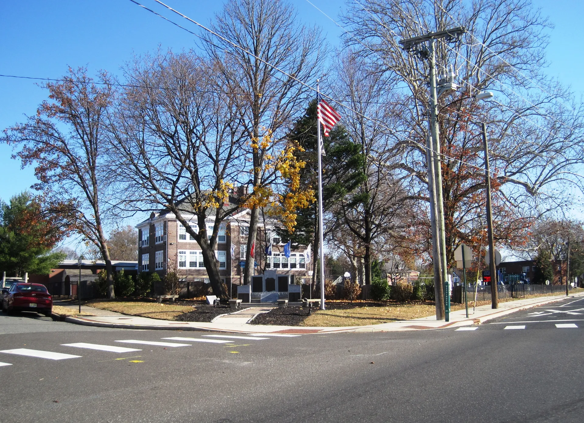 Laurel Springs' memorial and school share a corner lot with a flagpole and tall trees in late autumn.