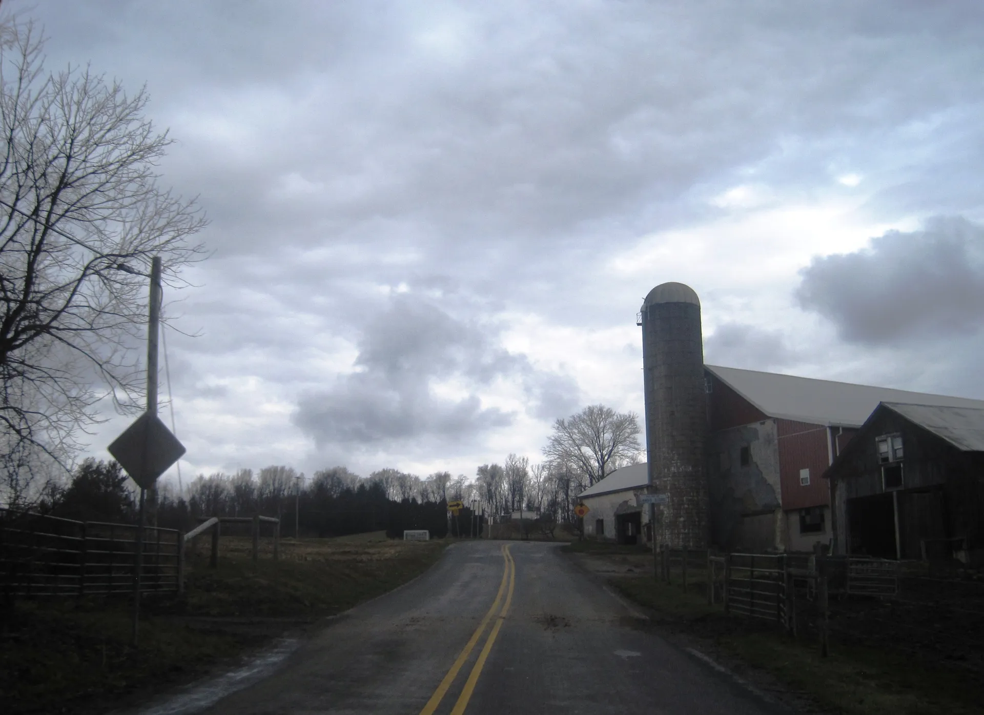 Landis Store Road passes a farm with a tall silo in the village of Landis Store in District Township on an overcast day.