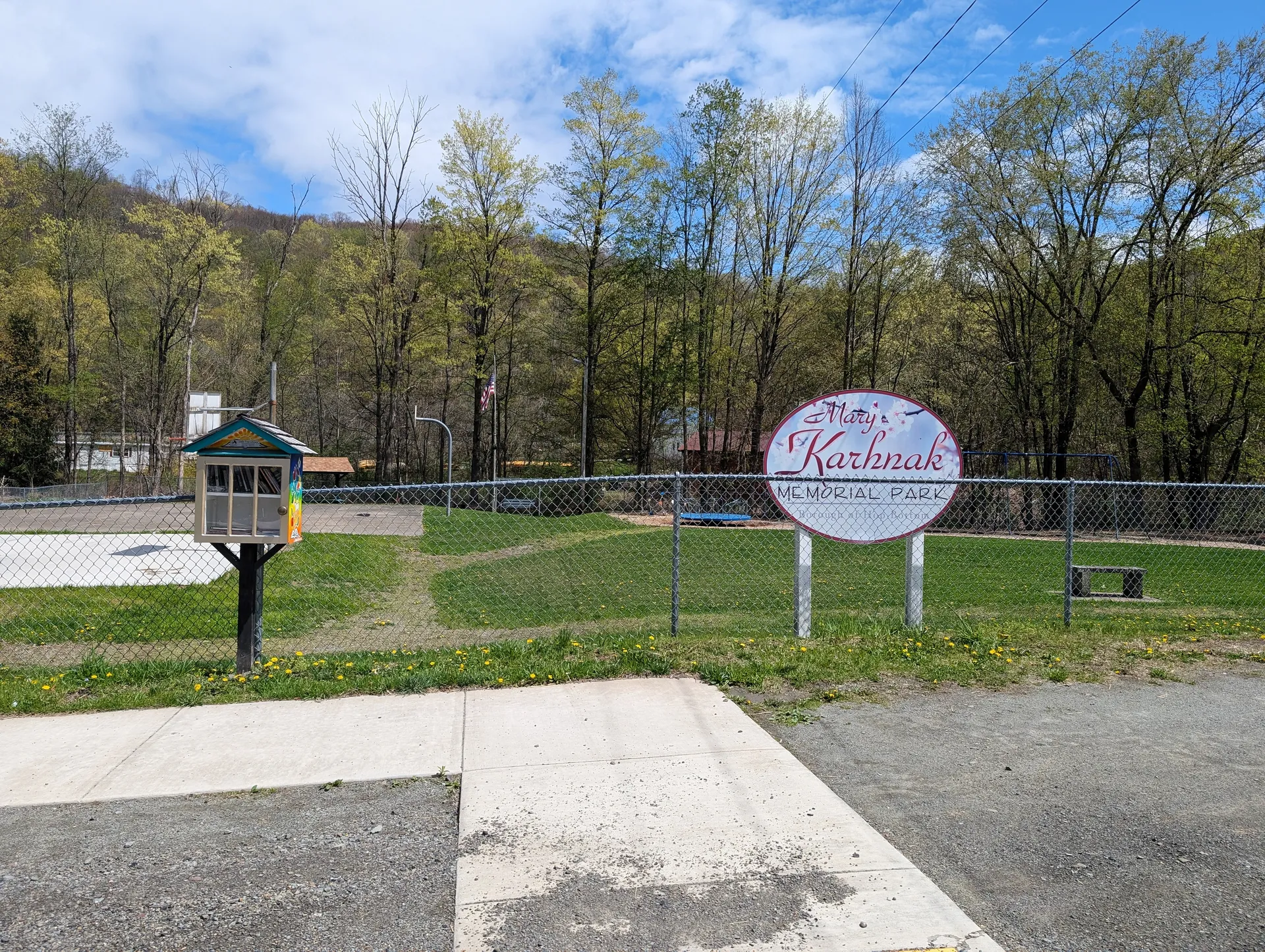 Mary Karhnak Memorial Park in Hop Bottom features a round welcome sign, lawn and a small pavilion against wooded hills.