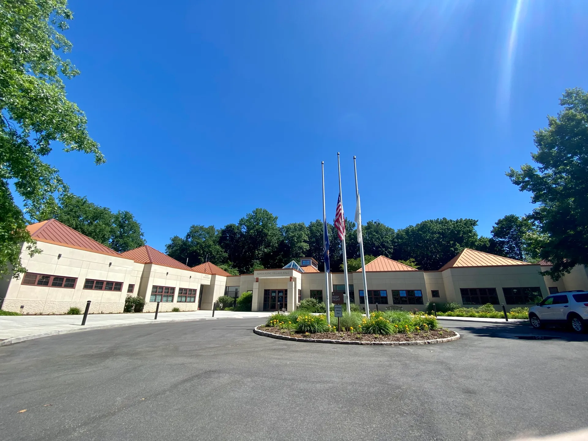 Kings Point Village Hall with flags and a landscaped circle in Kings Point, New York.