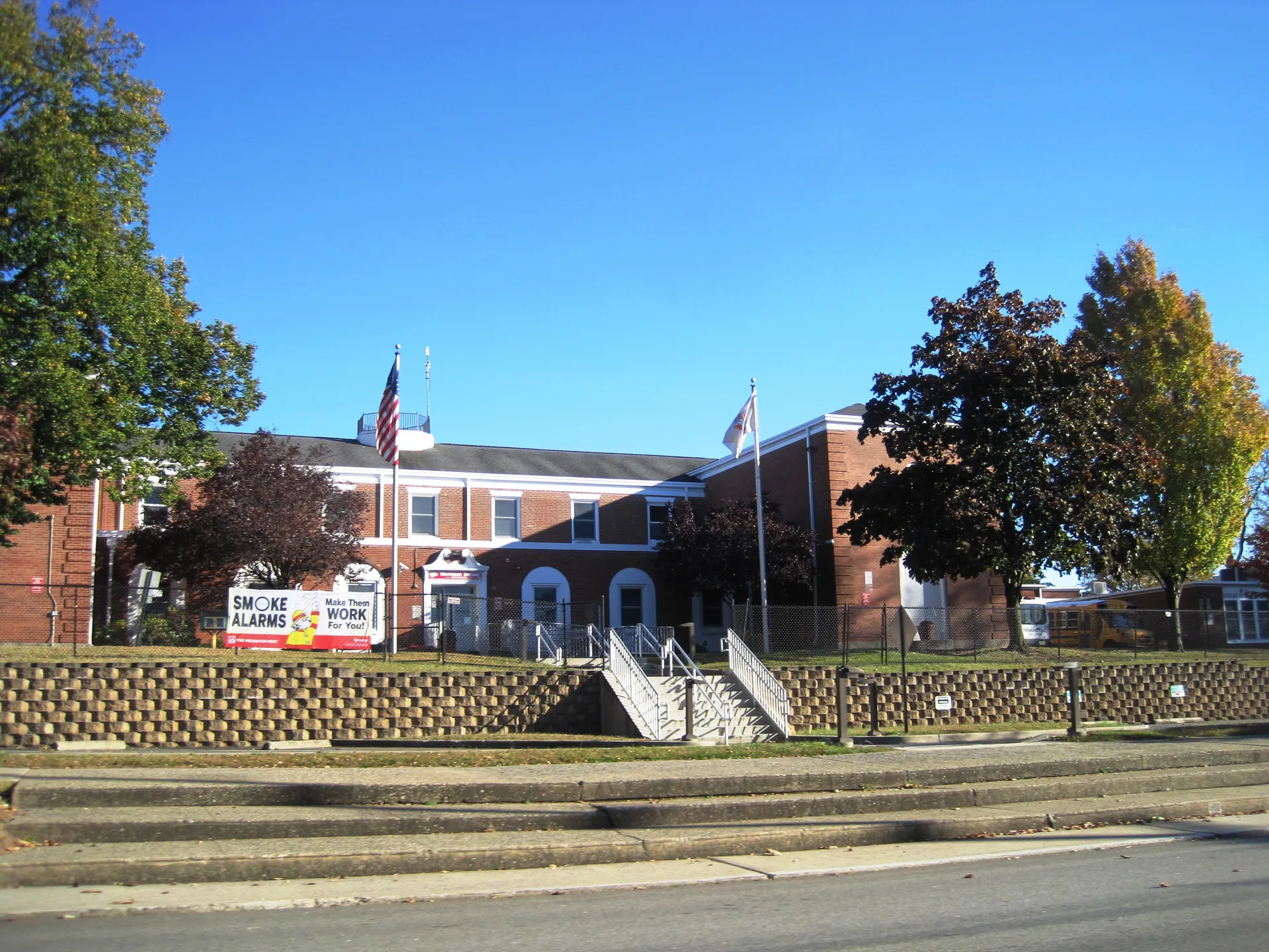Maywood Avenue School is a red brick building with a white cupola, set above stone steps and a lawn.