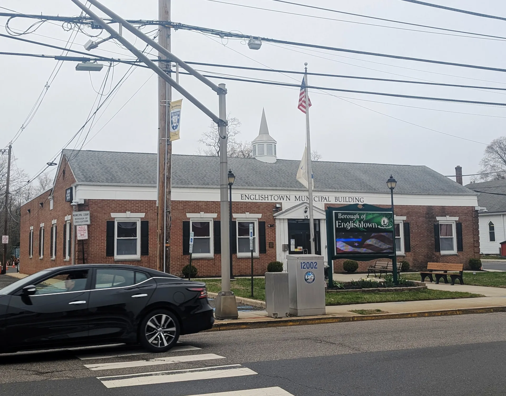 Englishtown's municipal building is a red brick structure with a white cupola, a flag and an electronic sign beside the street.