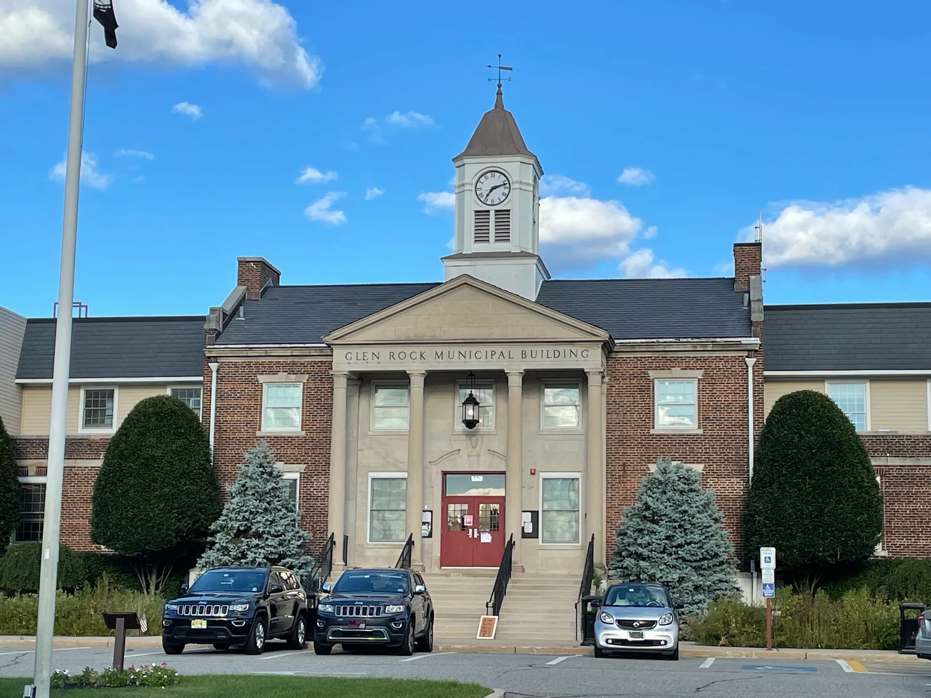 Glen Rock Borough Hall is a red brick colonial building with a white cupola and a pedimented entrance behind parked cars.