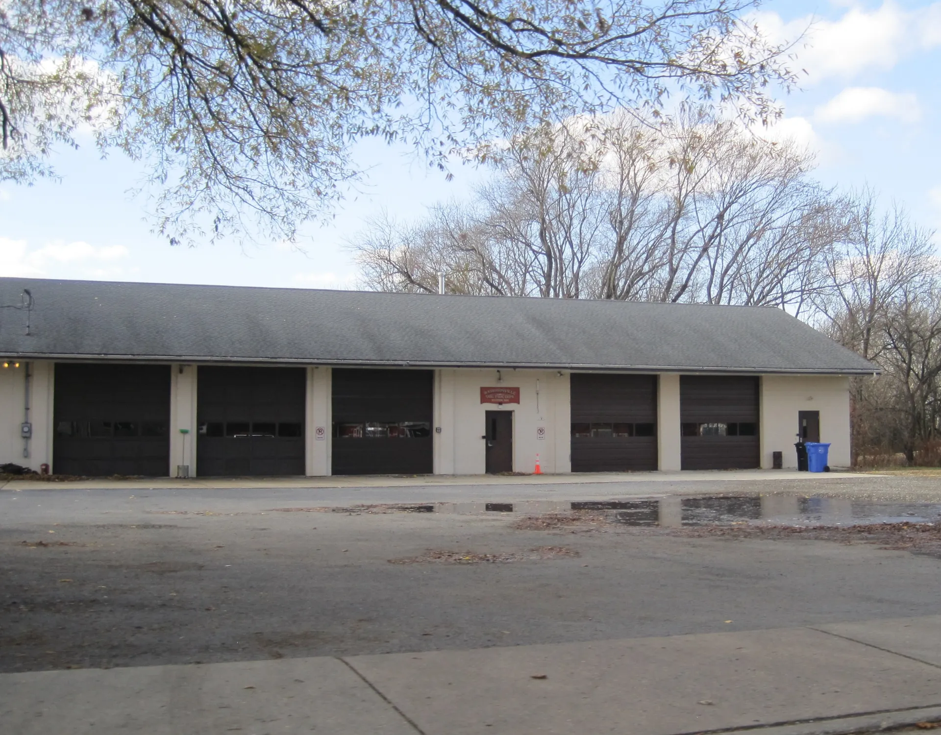 The Harrisonville fire department is a long low building with dark garage doors and a puddled lot in front.