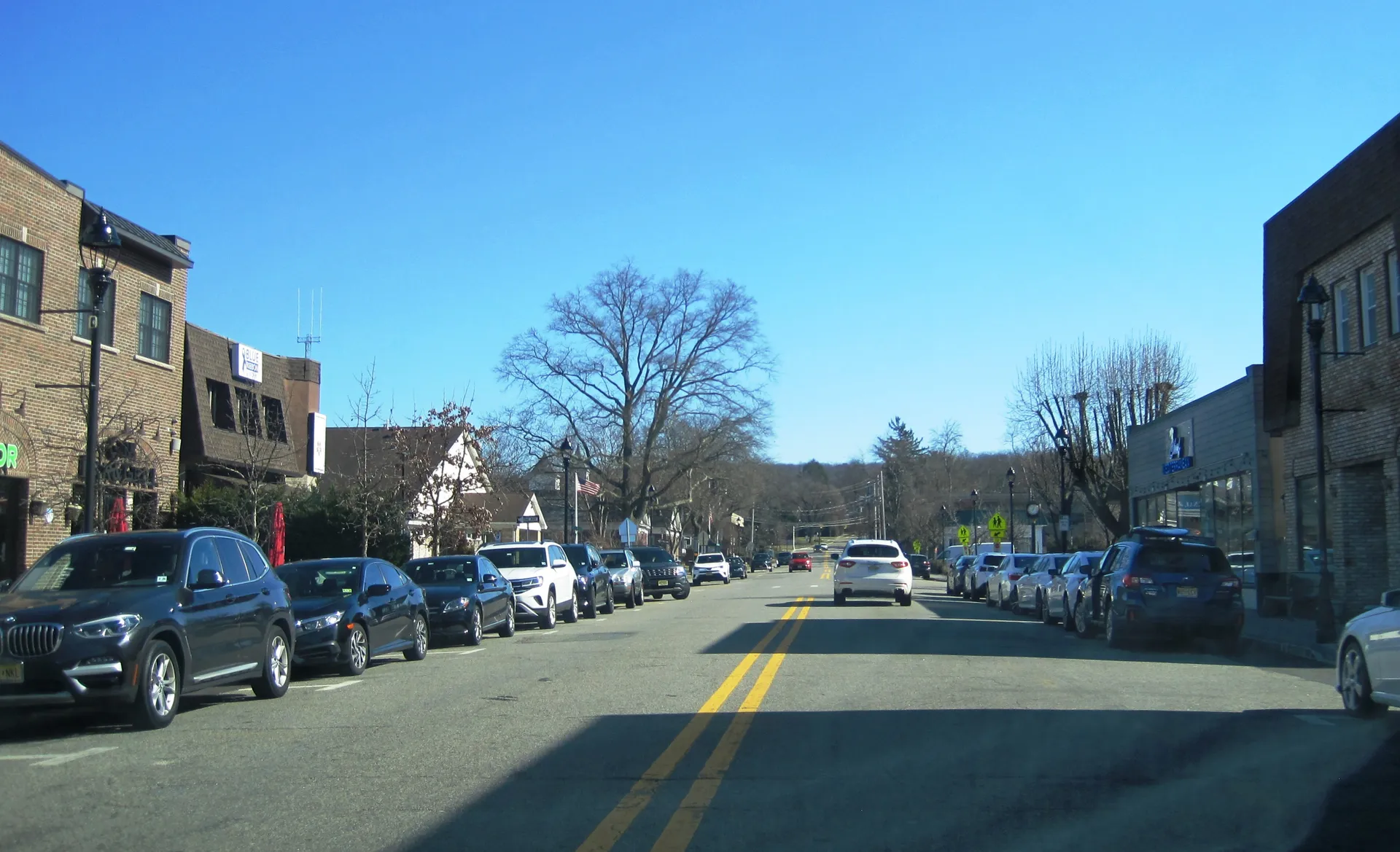 Union Avenue in Cresskill is a downtown street lined with parked cars and shops beneath tall bare trees on a clear day.