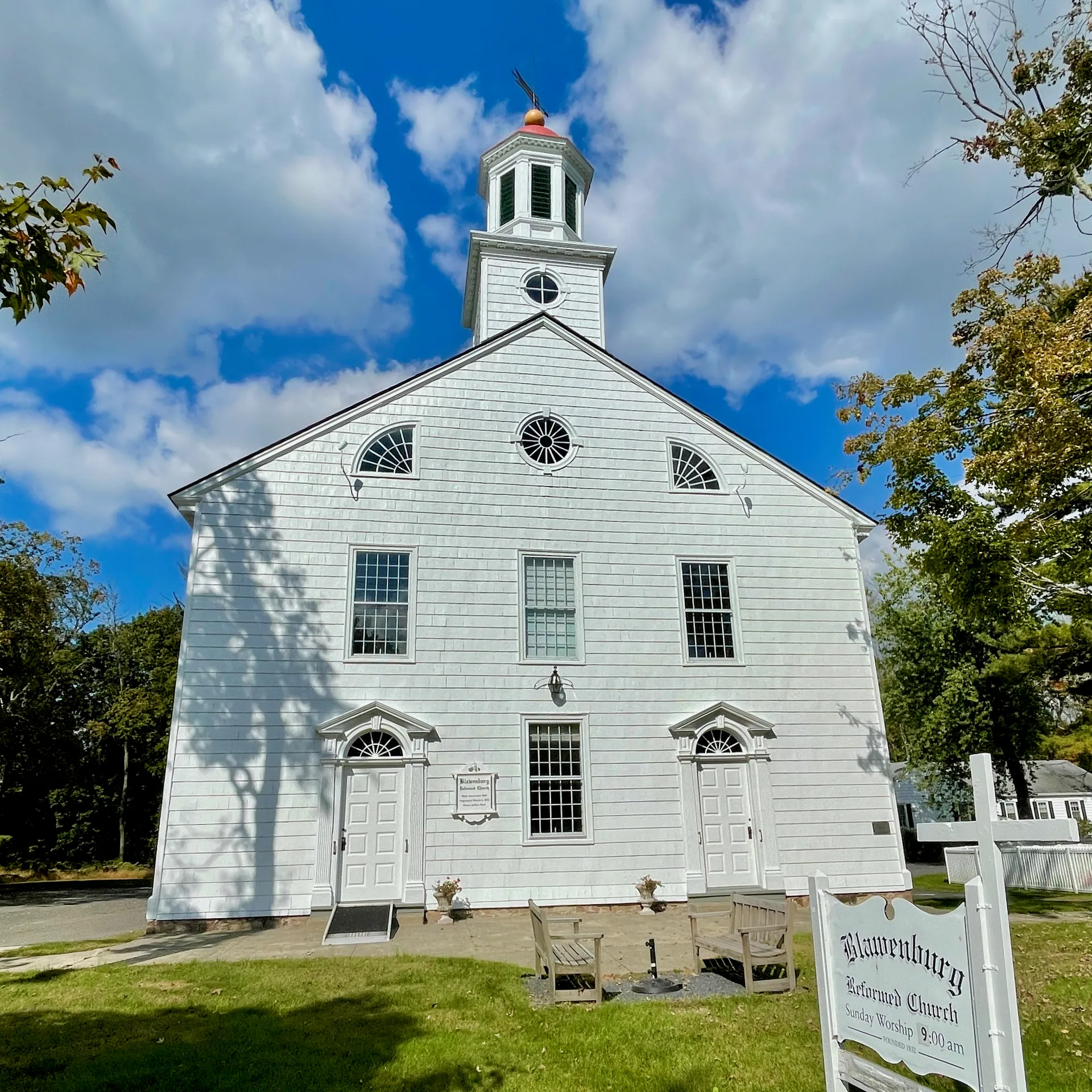 Blawenburg Reformed Church is a white clapboard church with a pedimented front and an open belfry against a blue sky.