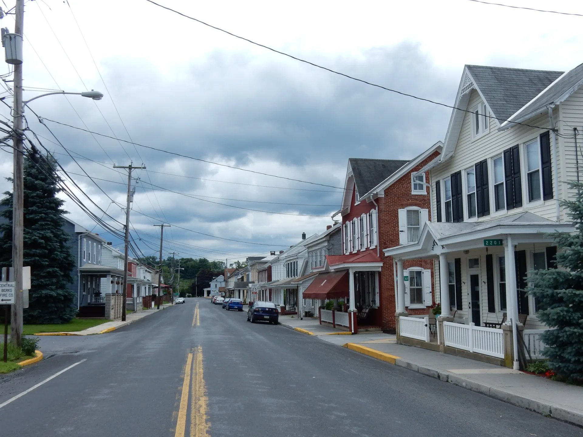 Brick and frame rowhouses with porches line Main Street in Centerport, a small Berks County borough, under a cloudy sky.