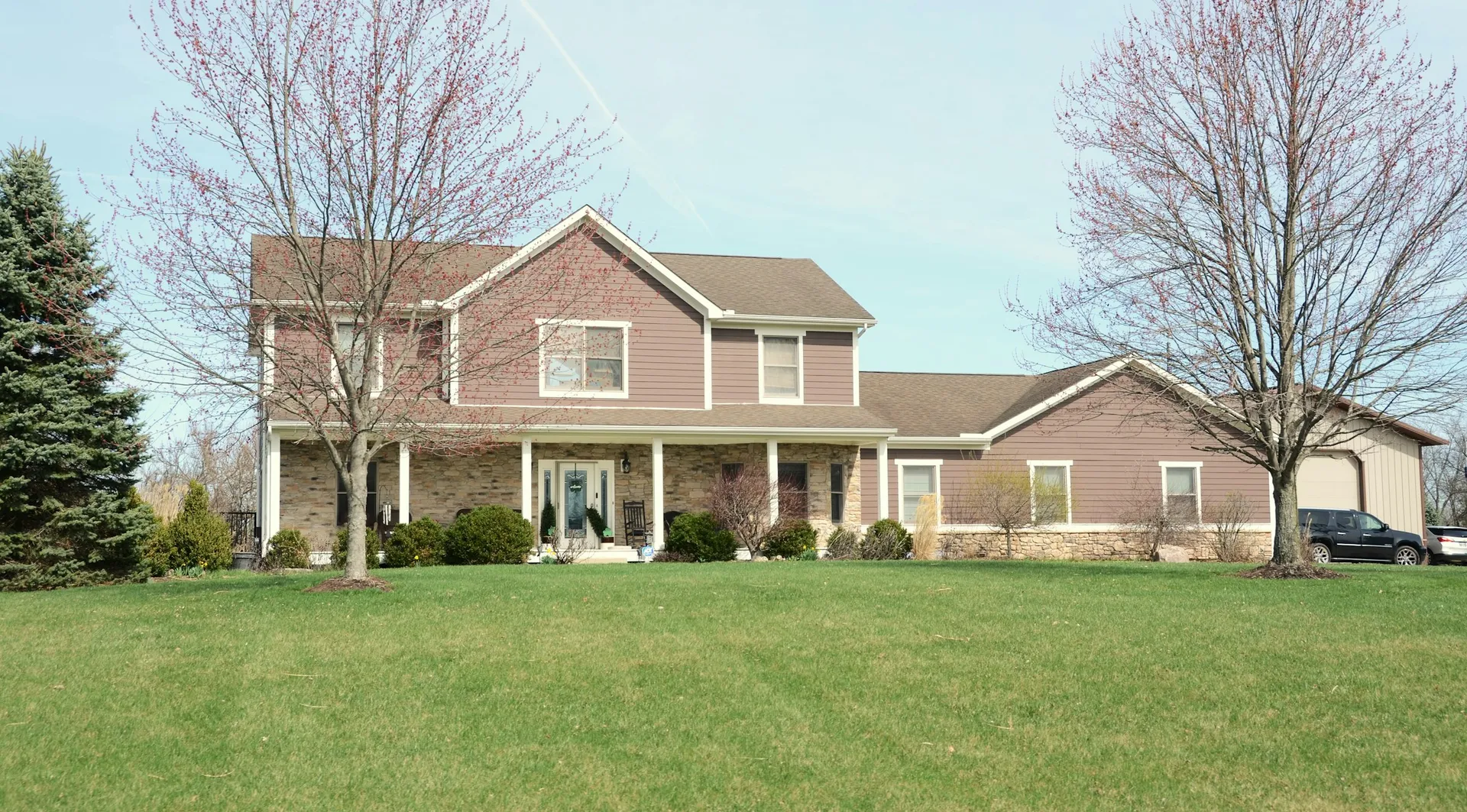 A suburban house with a front porch, green lawn and trees.