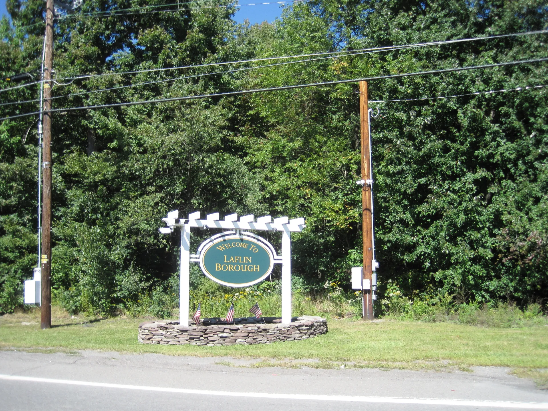A white pergola-style sign framed by green woods welcomes drivers to Laflin along Laflin Road near Route 315.