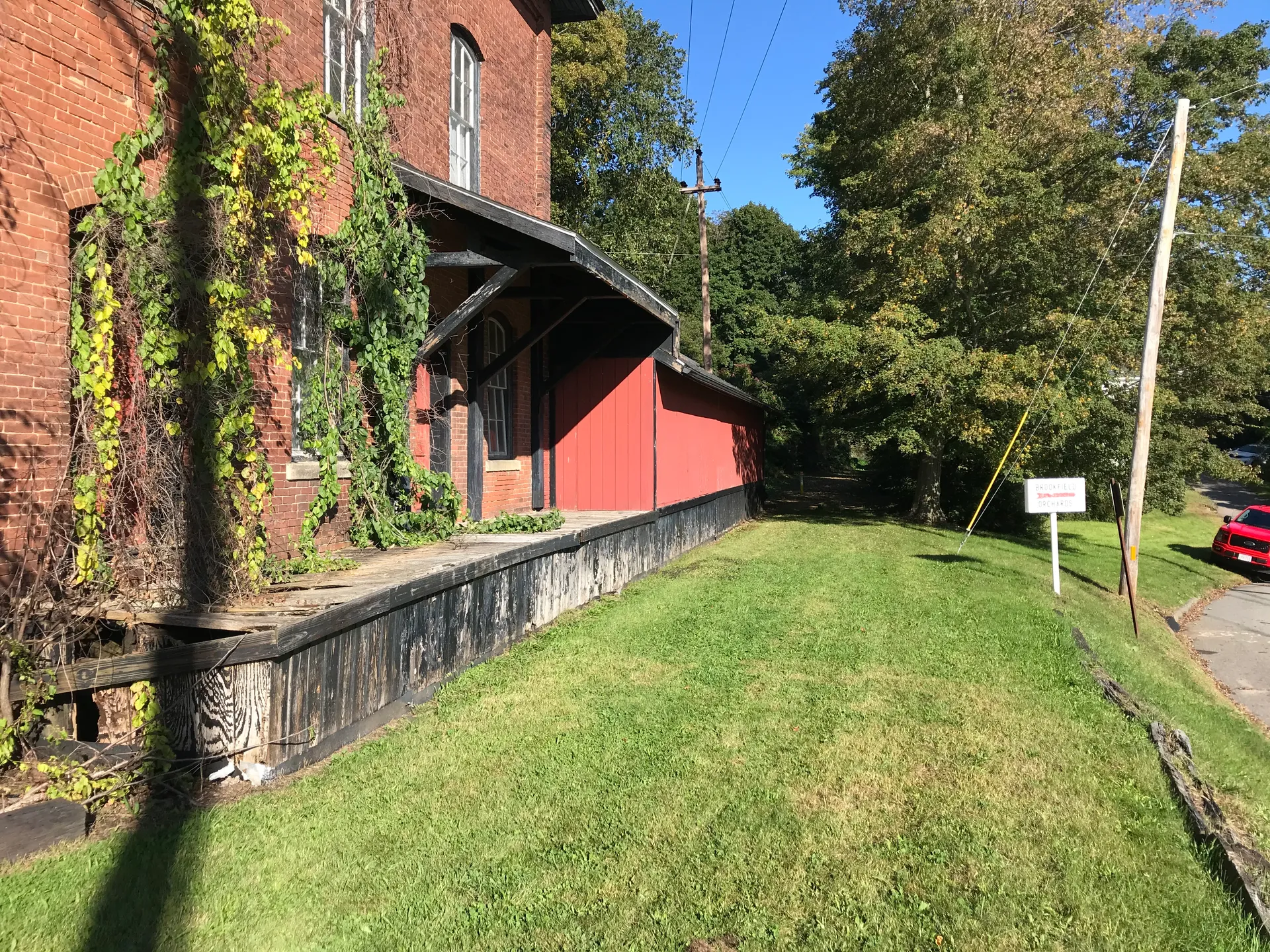 The old North Brookfield railroad station is a long red wooden depot with ivy climbing its brick end and a grassy yard beside it.