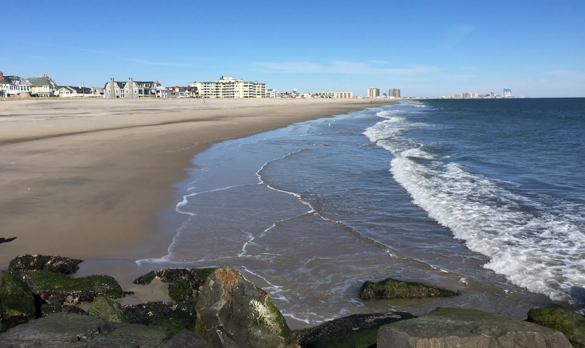 Waves wash onto the sandy shore of Longport Beach, with hotels and towers lining the coast beyond.