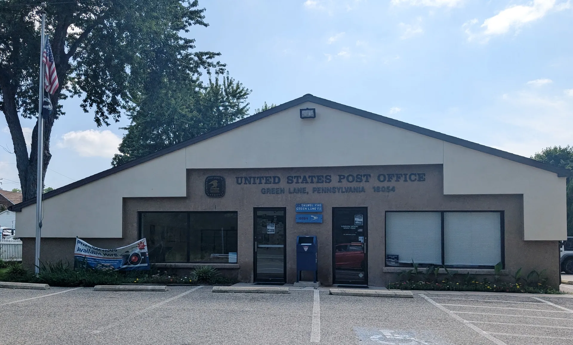 The Green Lane post office is a tan brick building with a gabled roof and large front windows.