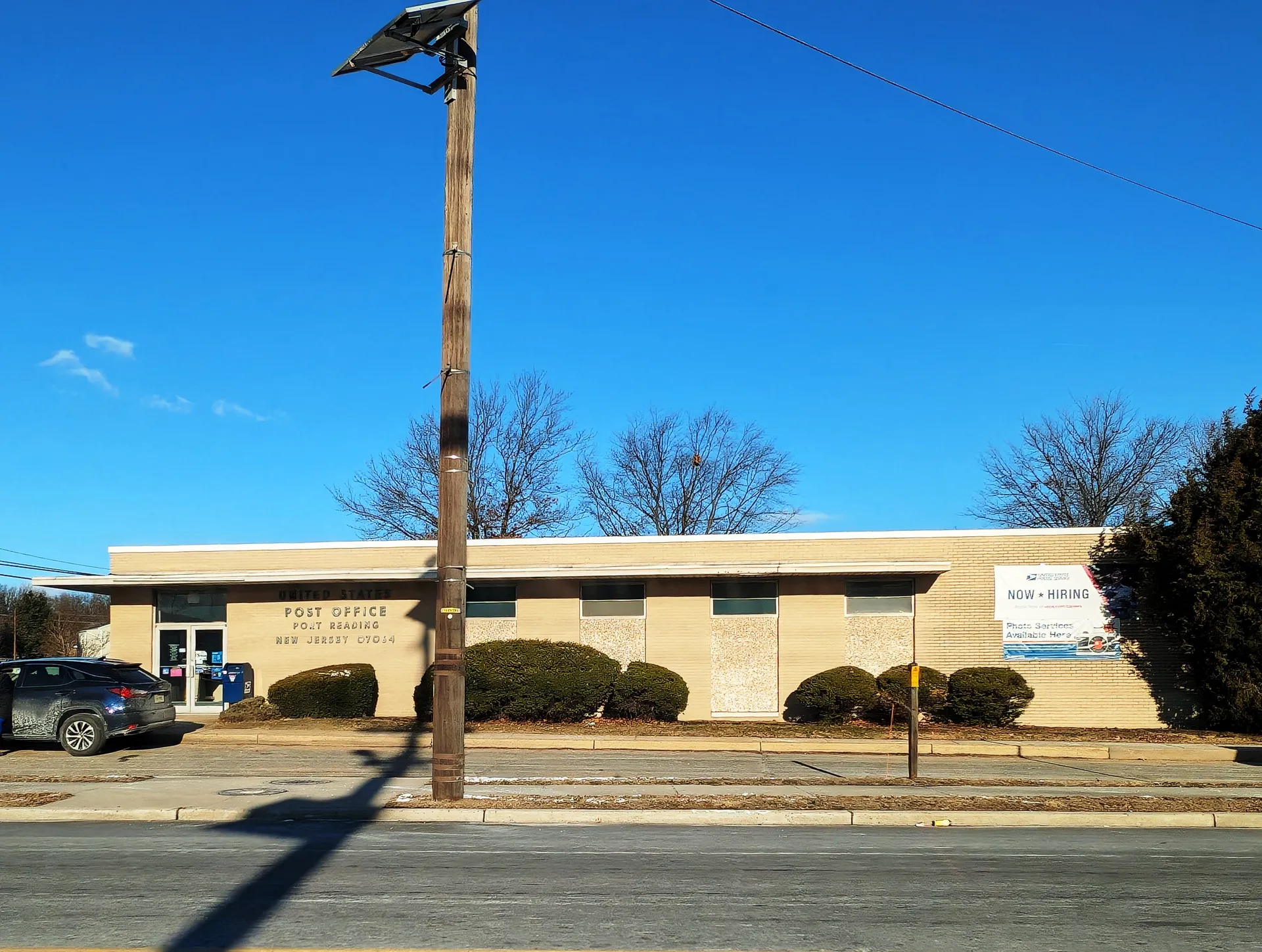 The Port Reading post office is a low tan brick building with shrubs along its front.