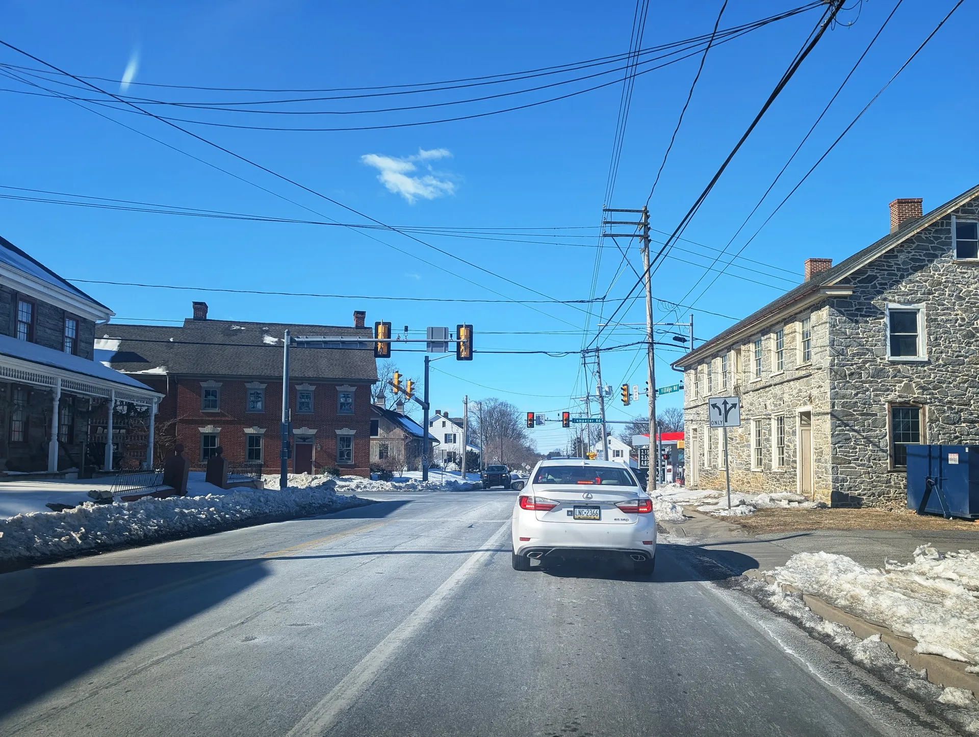 Village Road (Route 741) heads west through Lampeter at Lampeter Road, past a stone house and snow-edged sidewalks.