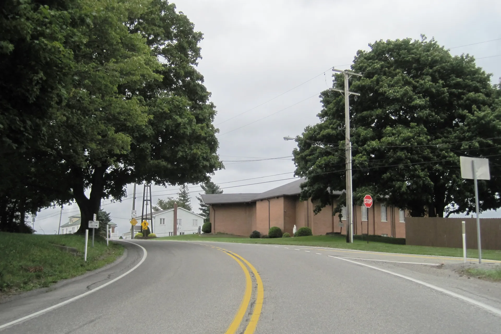 Colonel Drake Highway curves through Chest Springs past a low brick building and large shade trees.