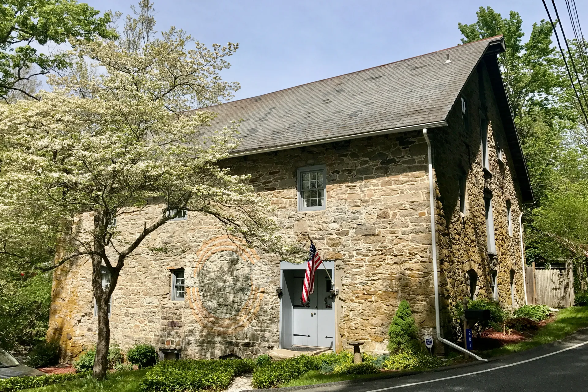 The Marksboro Grist Mill is a two-story fieldstone building with a steep roof and a flag beside the door.