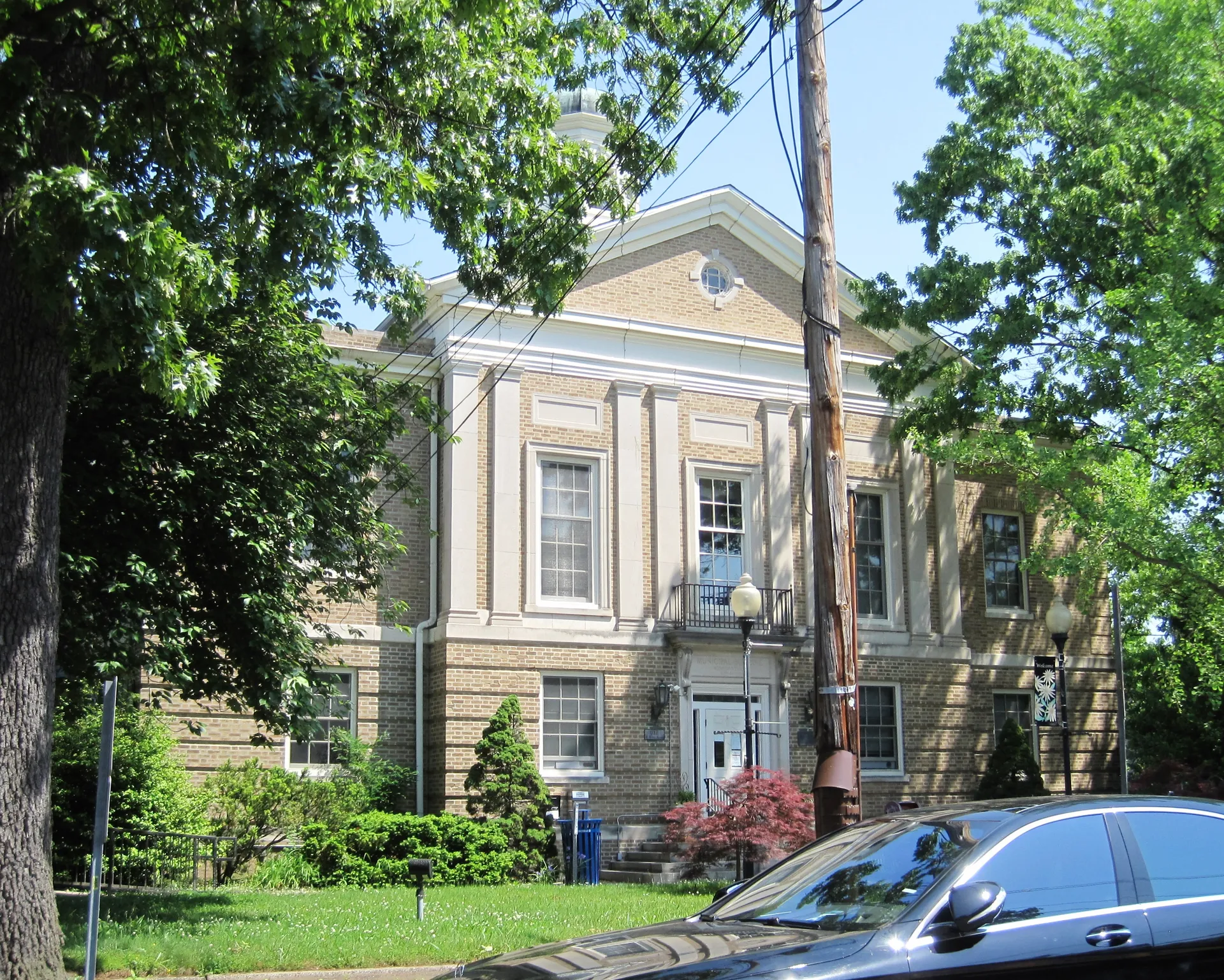 Merchantville's municipal building is a pale stone structure with a pediment and arched windows behind trees.