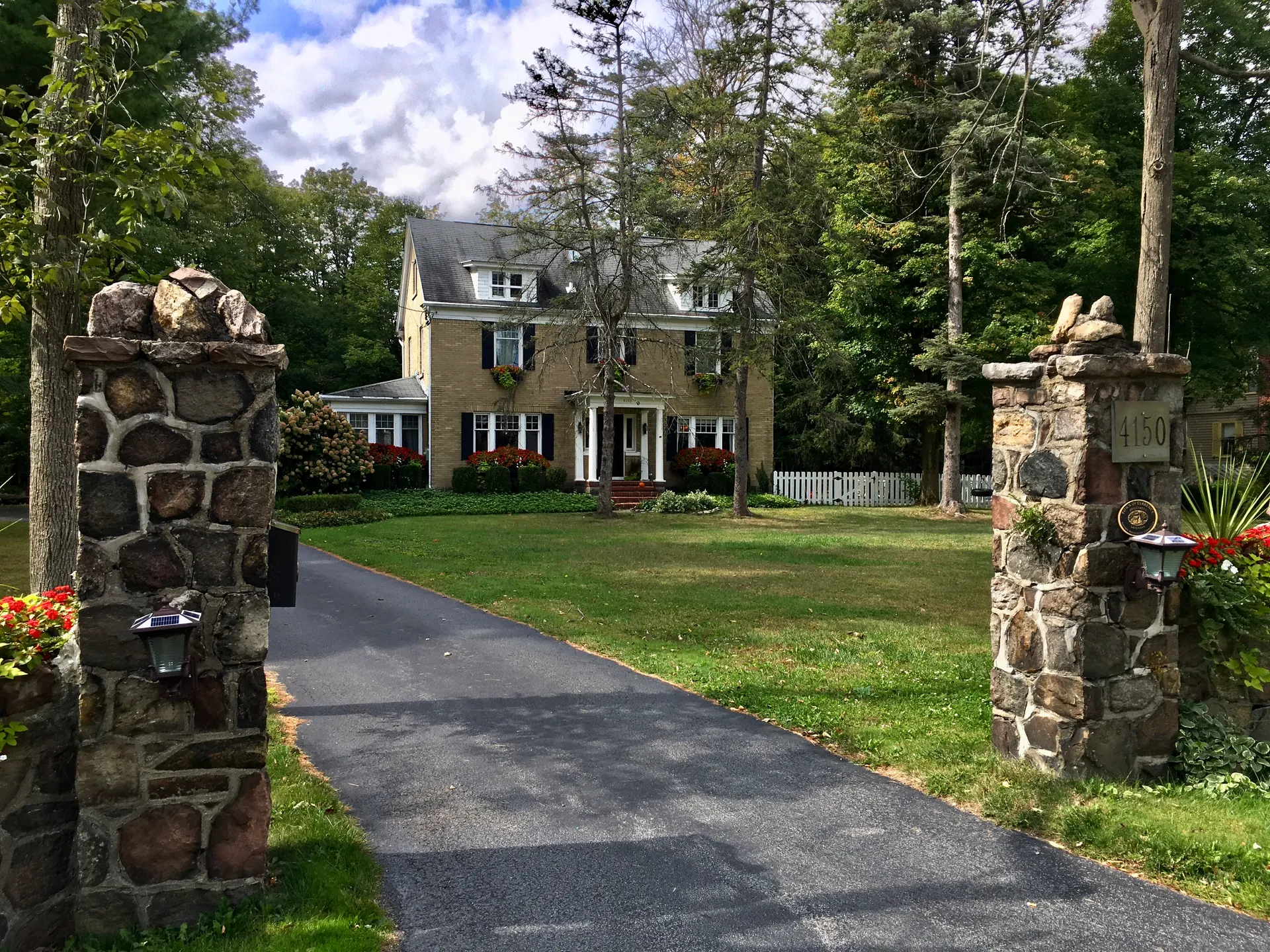 Historic house at the end of a drive framed by stone gateposts on Harris Hill Road in Clarence, New York.