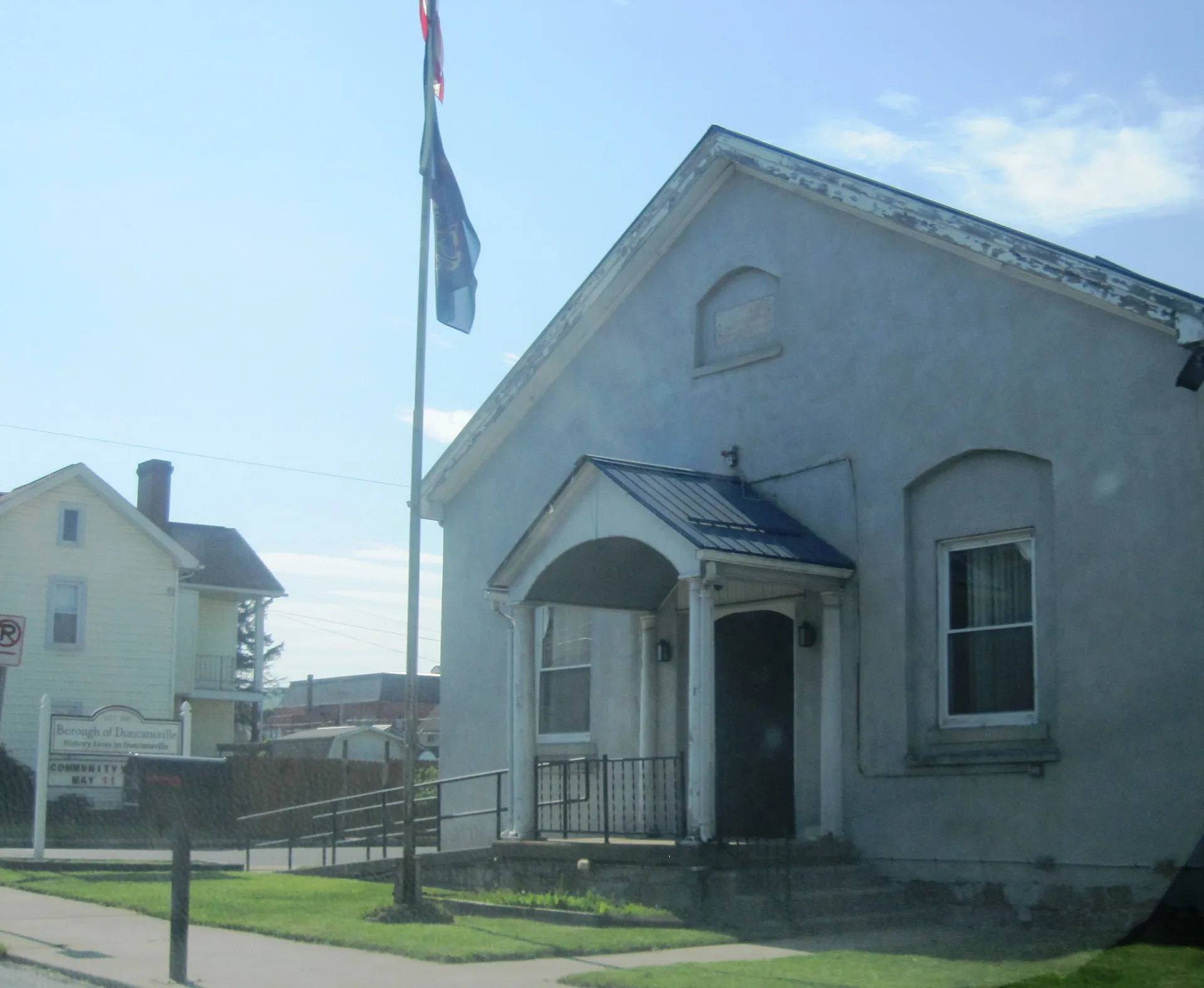 Duncansville's borough hall is a gray clapboard building with an arched gable window and a covered entry beside a flagpole.