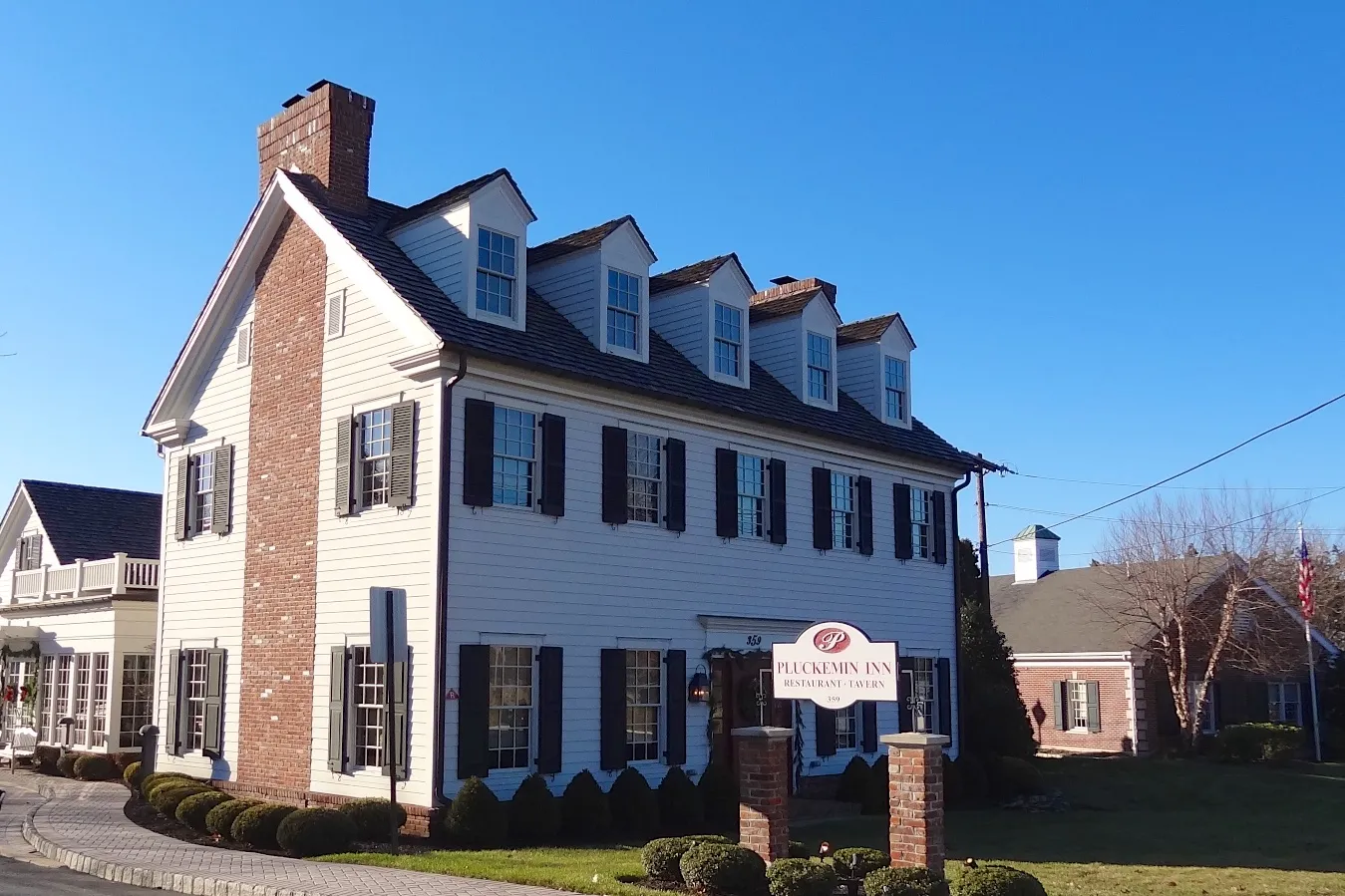 The Pluckemin Inn Tavern is a white three-story colonial building with black shutters and dormers.