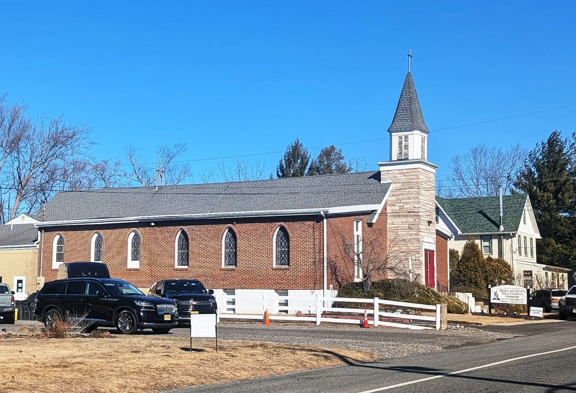 Iglesia Adventista in Gibbsboro is a red brick church with a white steeple and a white rail fence along its parking area.