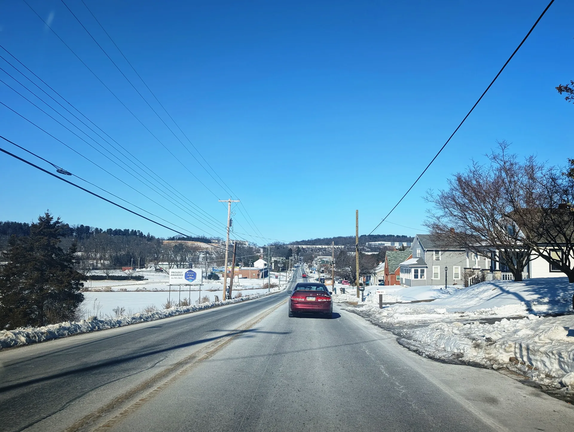 North George Street (Route 181) runs through Emigsville past snowy lawns and brick buildings on a sunny winter day.