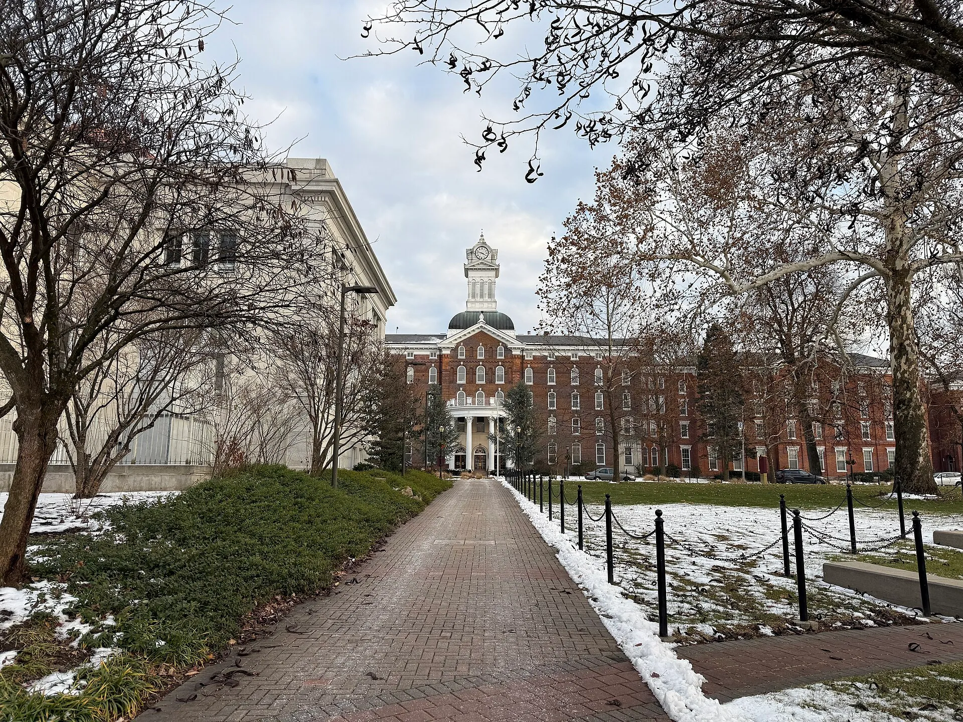 A brick walkway through Alumni Plaza frames Old Main at Kutztown University, with its white cupola beyond bare trees.