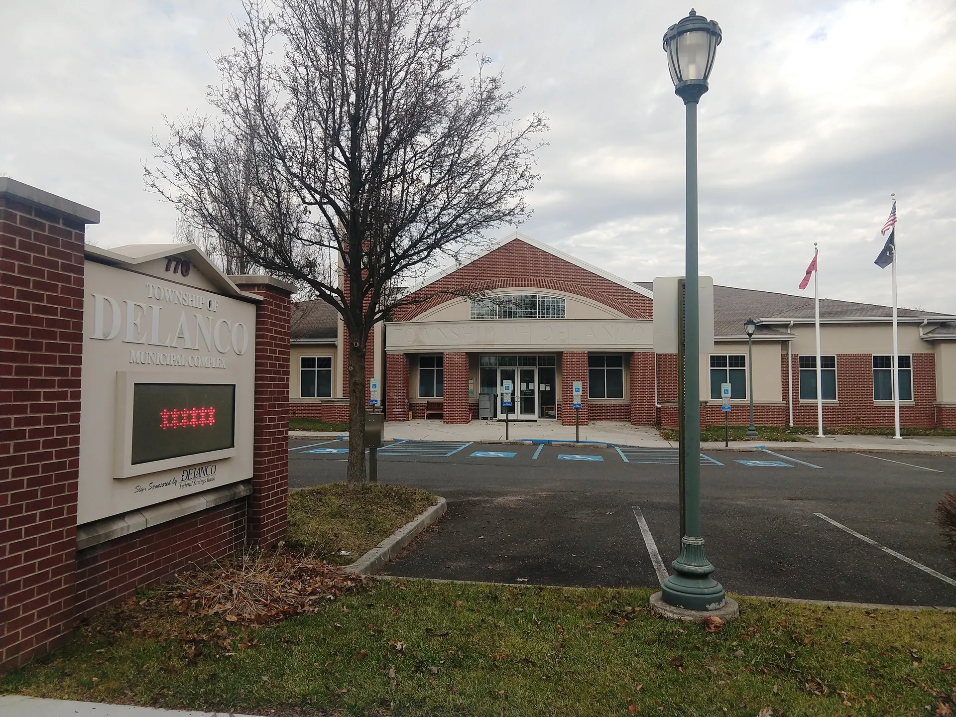 The Delanco Township municipal building is a single-story red brick structure with a white gabled entry and a lamppost in front.