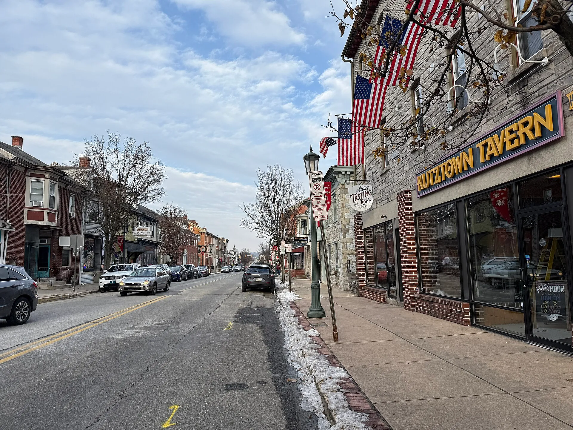 Main Street in Kutztown passes Whiteoak Street with a brick tavern, flags and storefronts along the sidewalk.