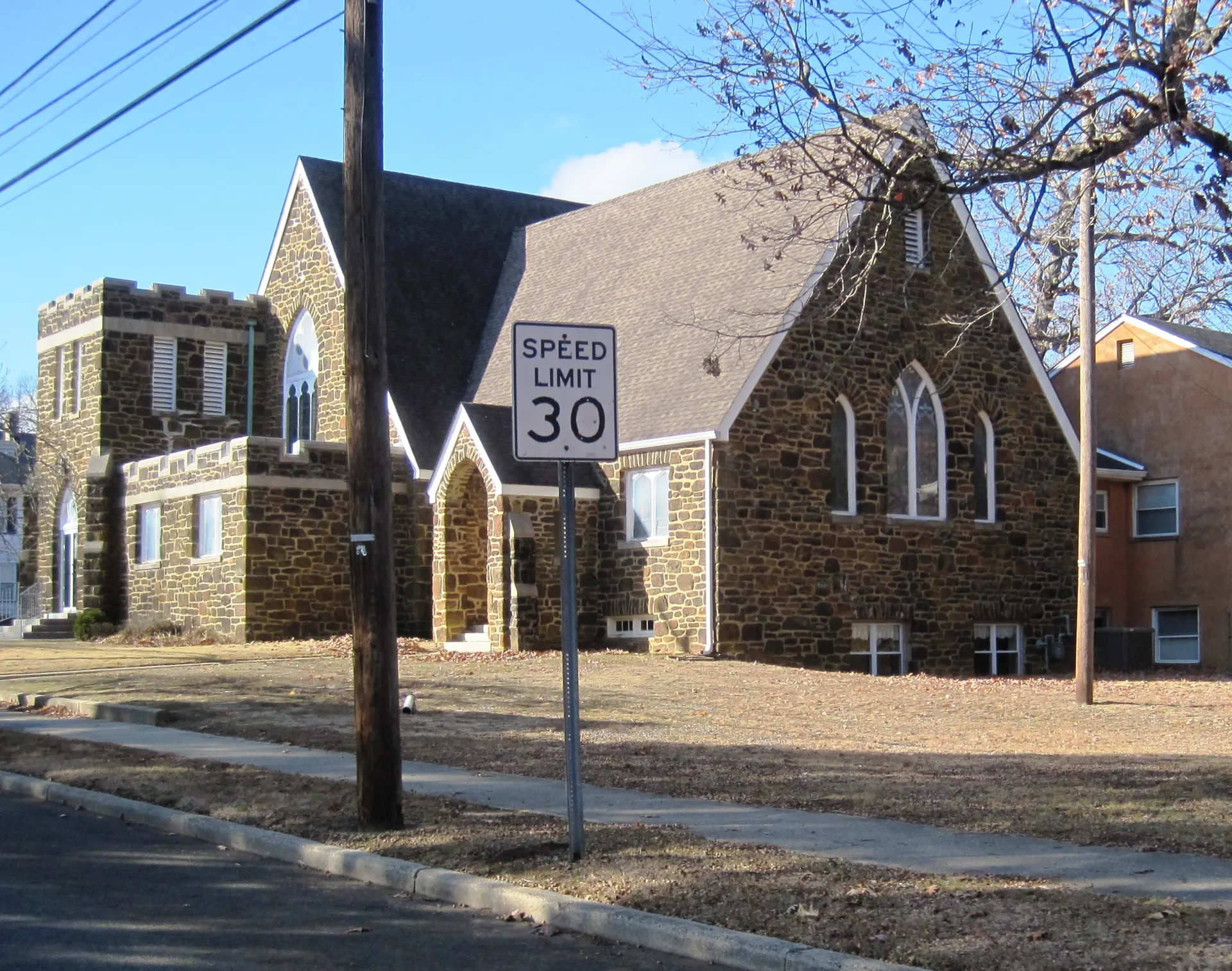 First Baptist Church in Newfield is a stone church with a steep gable and an arched window behind a speed sign.