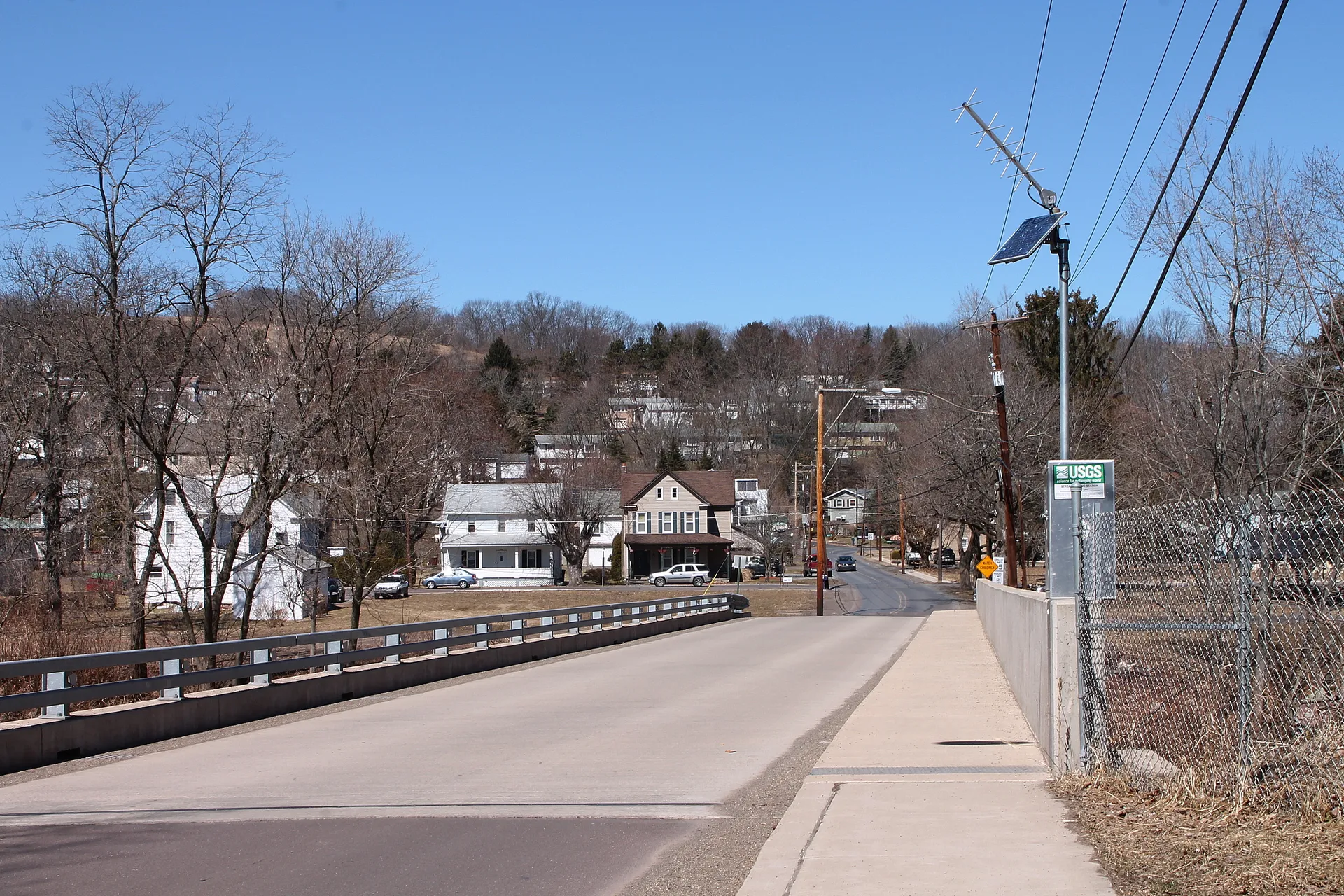 Houses of Fernville climb a wooded hillside beyond a bridge, viewed from the Bloomsburg side.