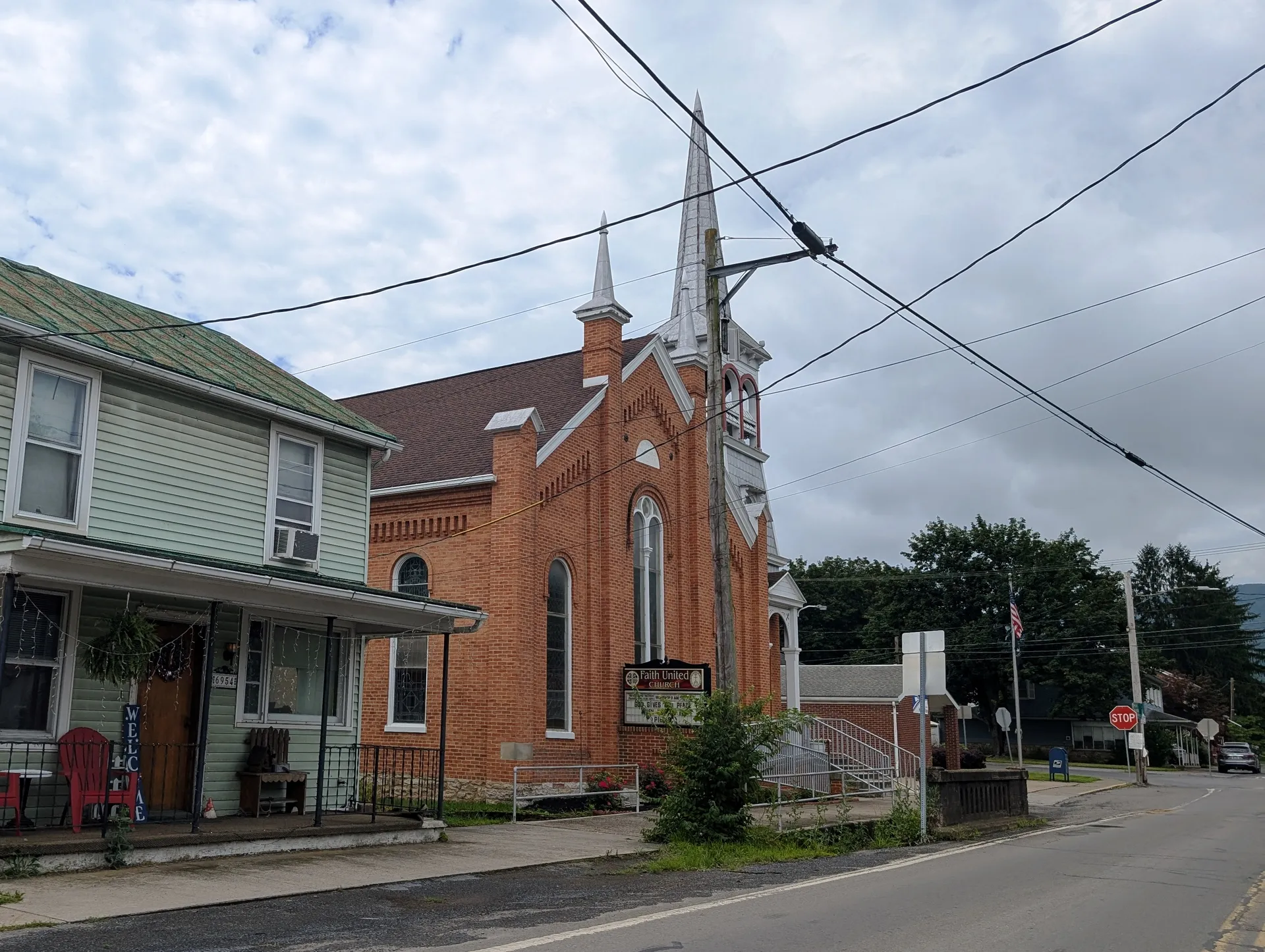 Faith United Church in Ickesburg, Perry County, is a red-brick church with a tall spire beside a porch-fronted house.